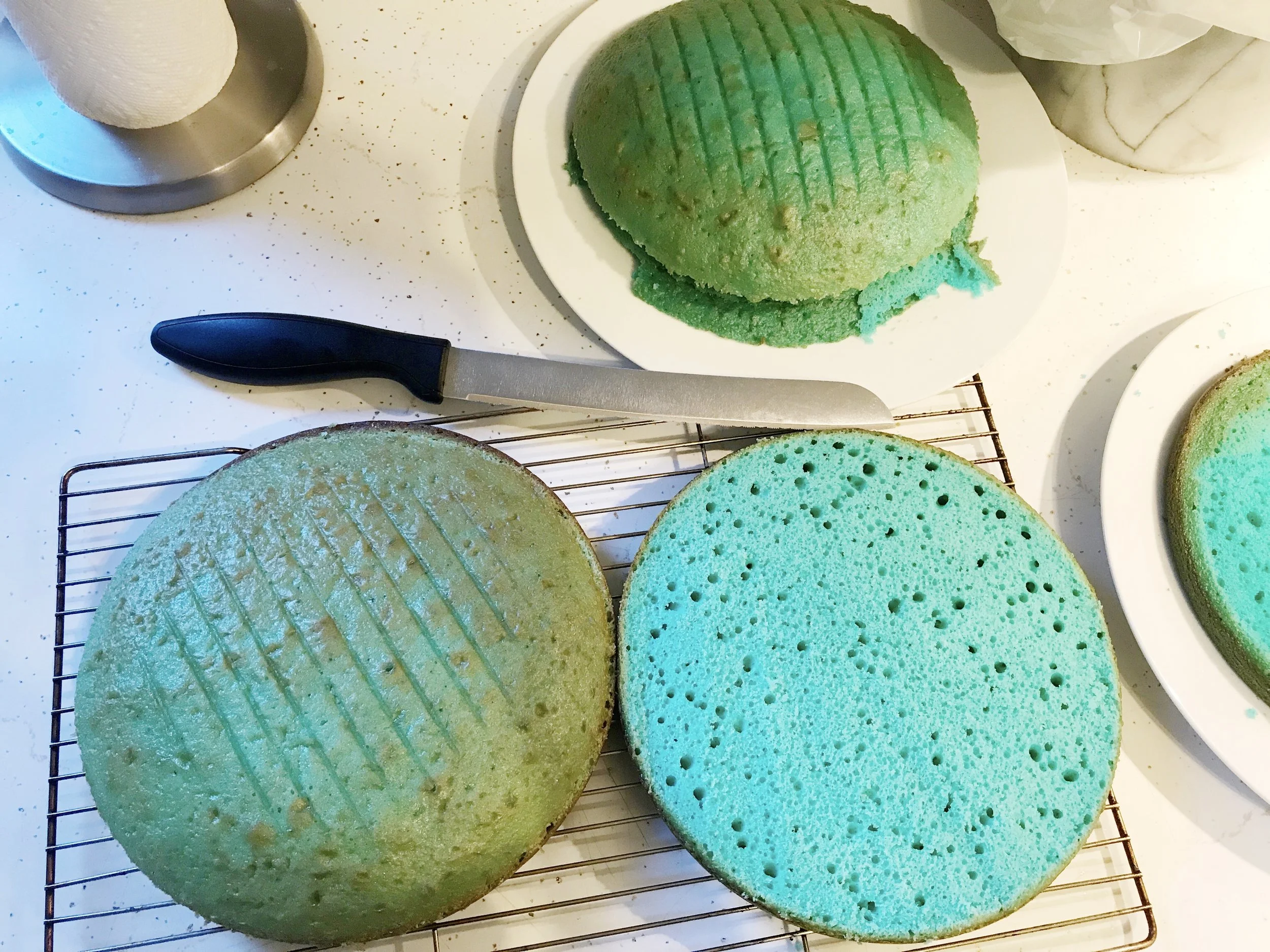 Cutting the domes off the tops of the baked cakes with a bread knife. I used the French Vanilla flavour of cake mix which had a yellowish tint to it, resulting in a greenish-blue cake exterior. Thankfully this didn't affect the colour on the inside, but if I were to bake this again I would use the White cake mix. 
