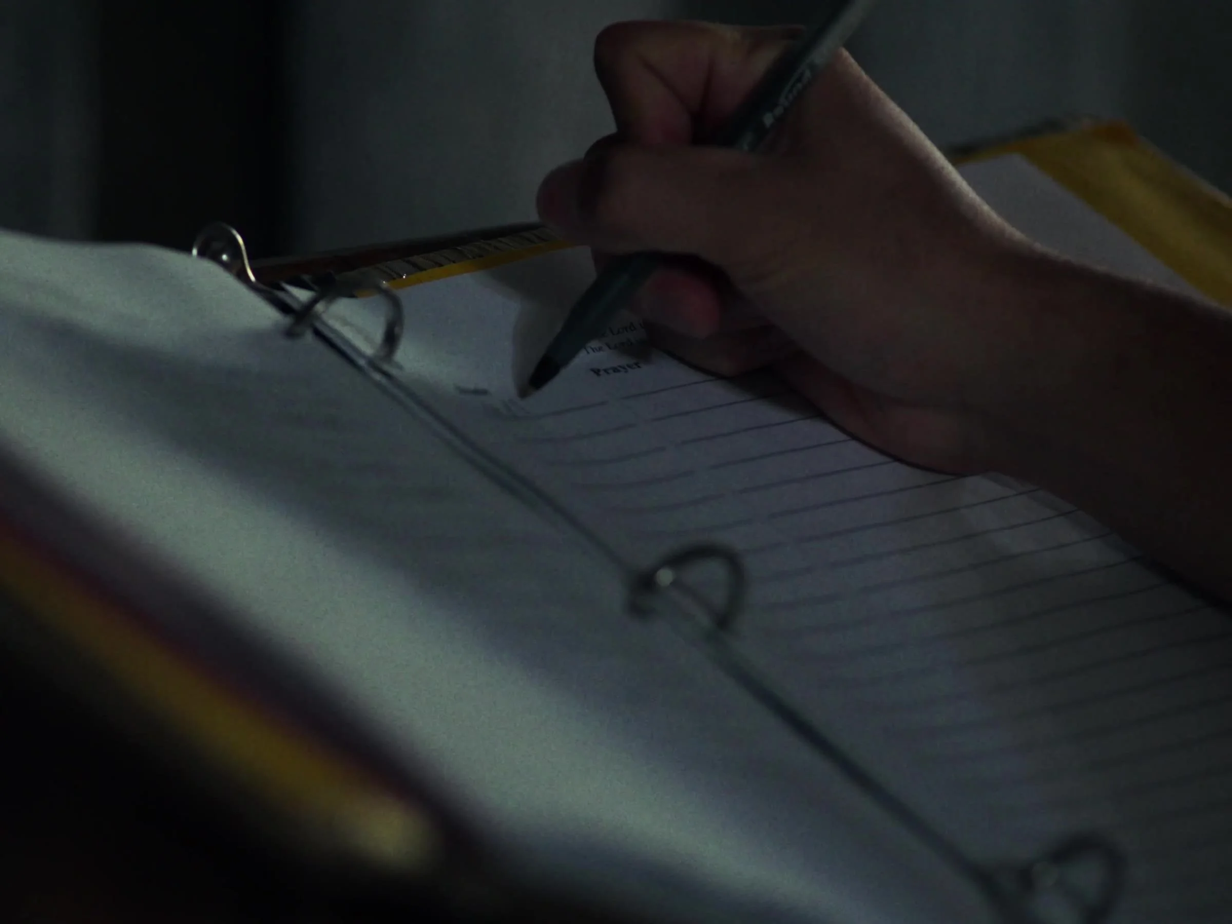 A hand writing prayer intentions in the book at the Newman Hall chapel. Photo by @reagancalaguasfilm