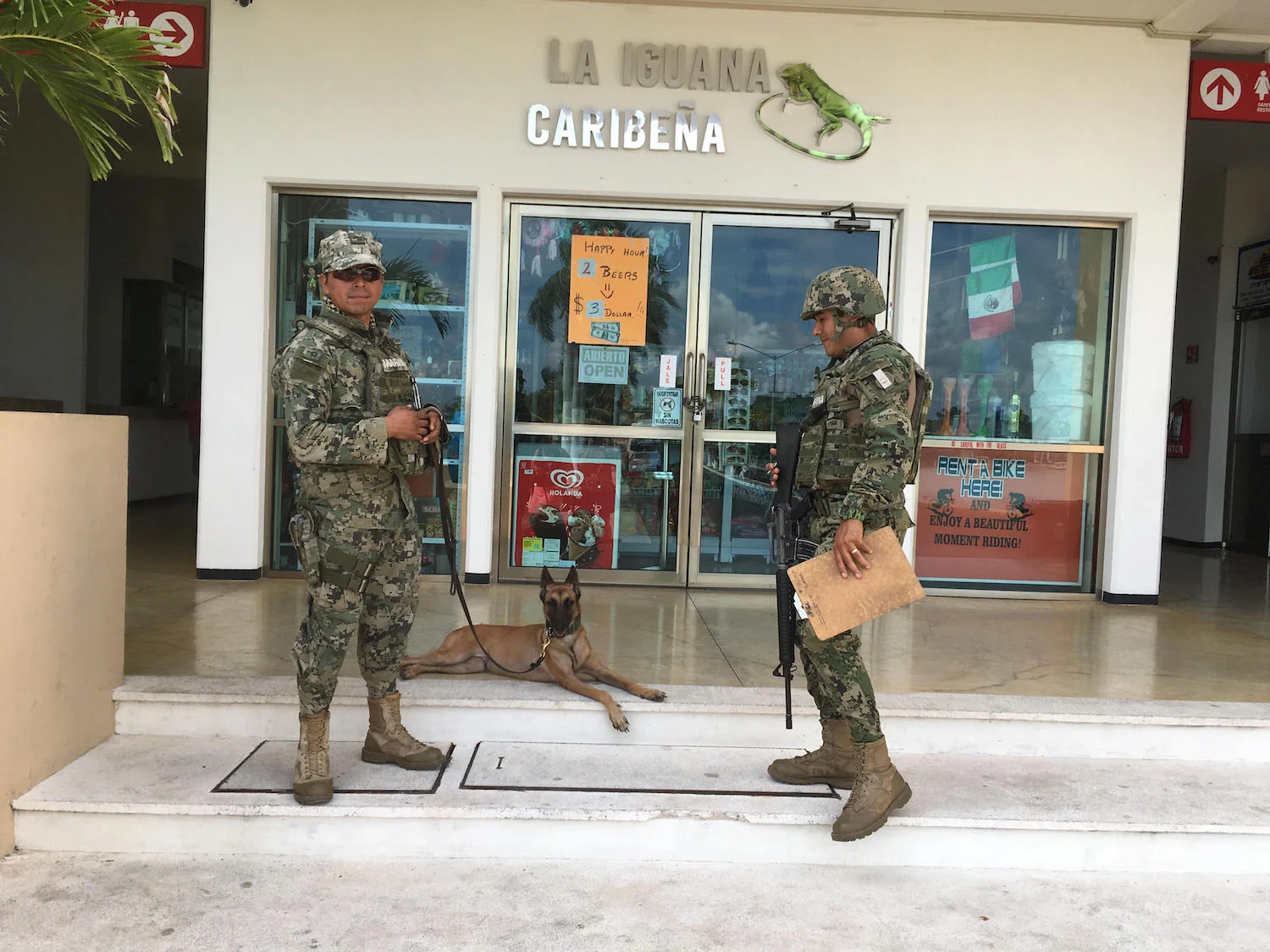 The soldiers use a trained dog for sniffing drugs in people's luggage.