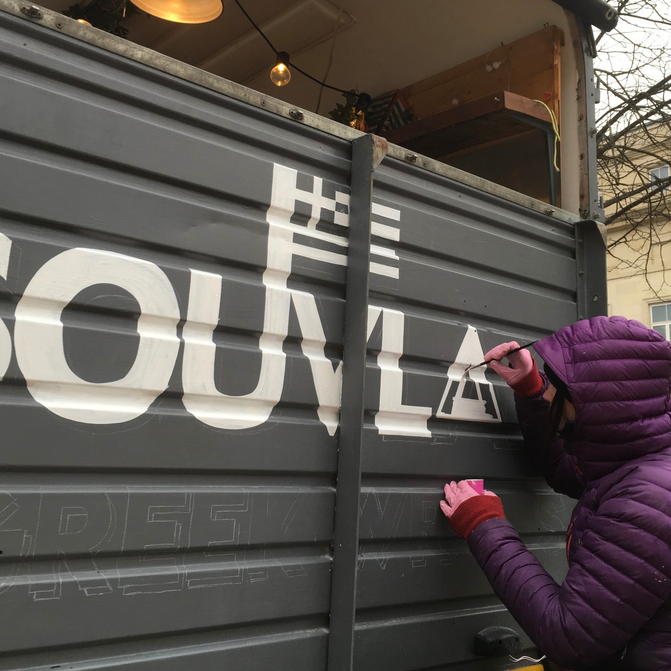 Painting progress of a food truck spelling 'Souvlaki' on ridged metal.