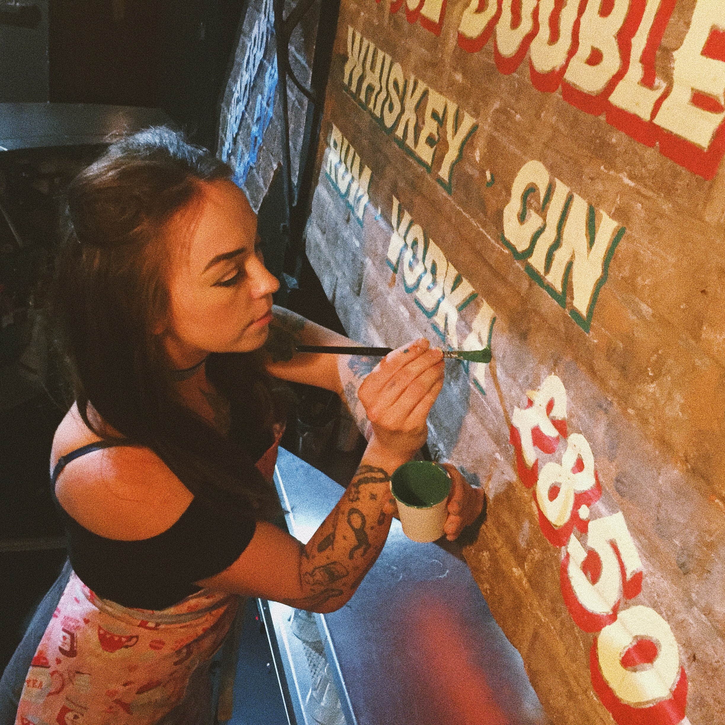 Female sign writer hand painting retro style signs on rough brick.
