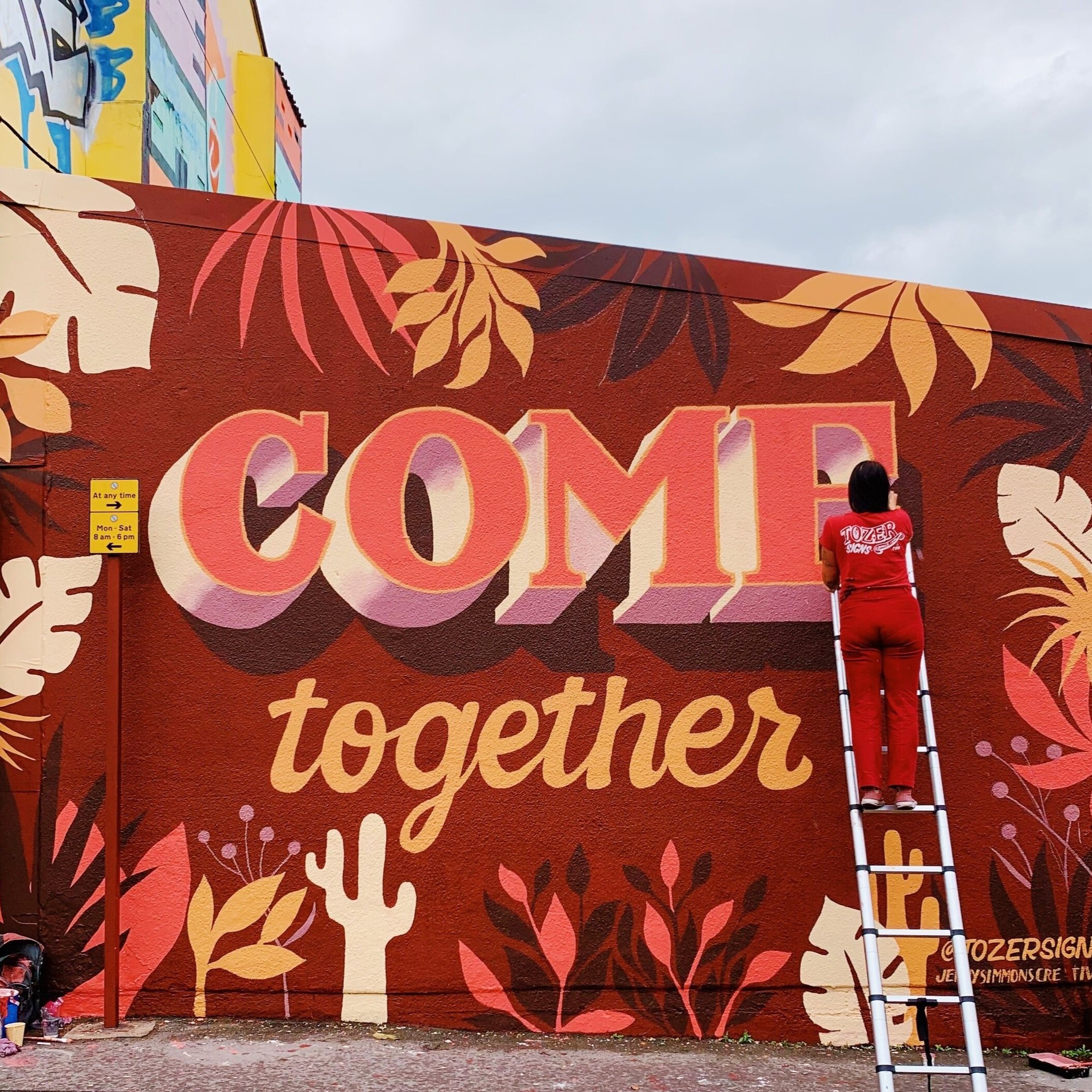 Hand-painted mural spelling 'Come Together' in reds, pinks and oranges.