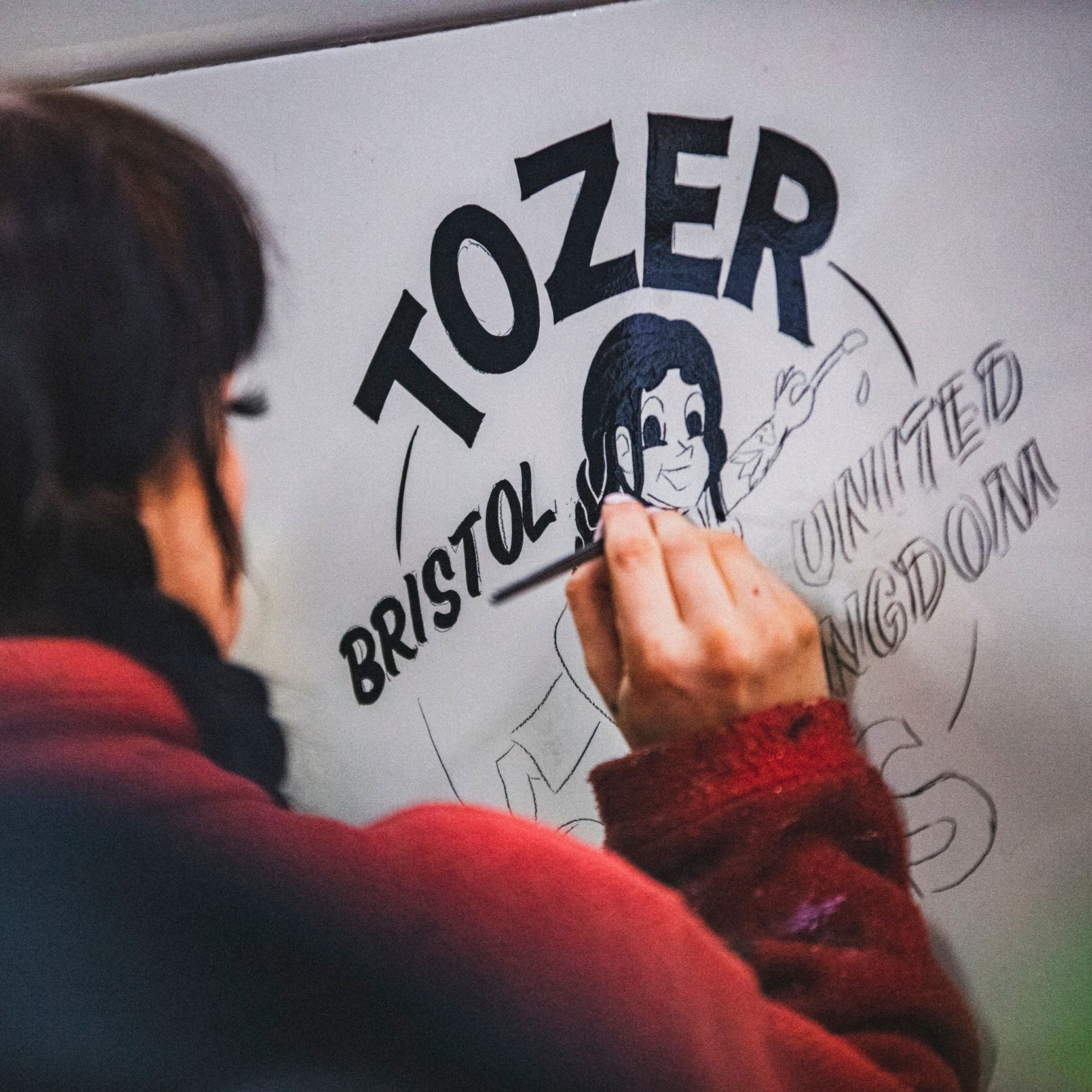Tozer Signs painting her own logo on a vintage car.