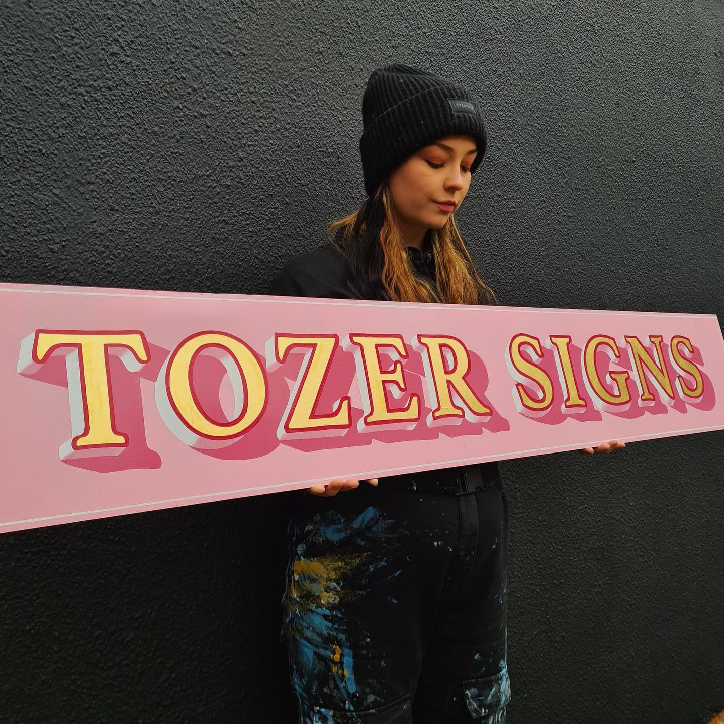 Tozer Signs holding a namesake gilded and painted sign.