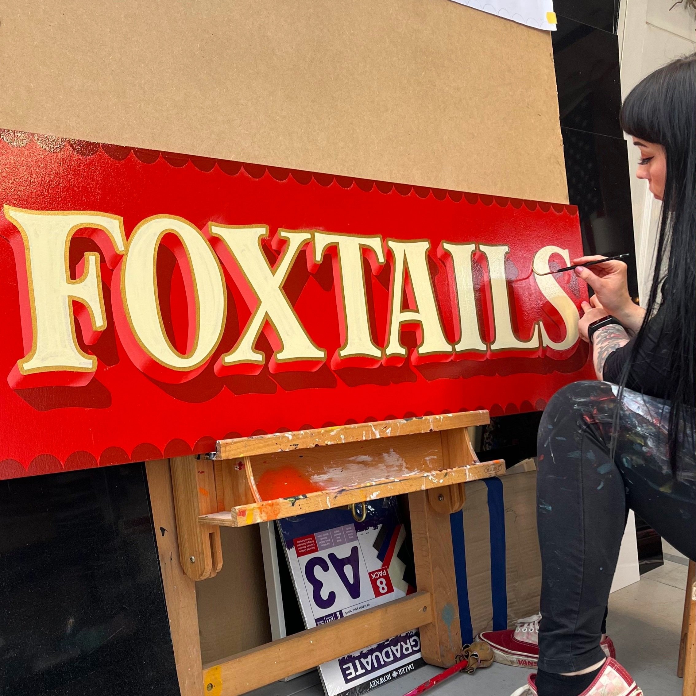 Progress photo of a red and cream sign spelling 'Foxtails'