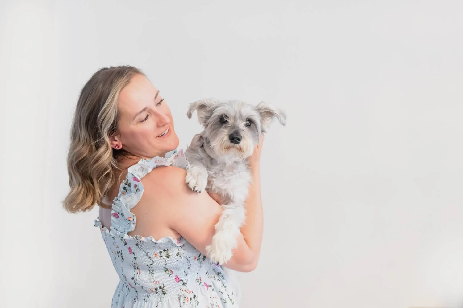 A lady holding a small dog and smiling at him with love