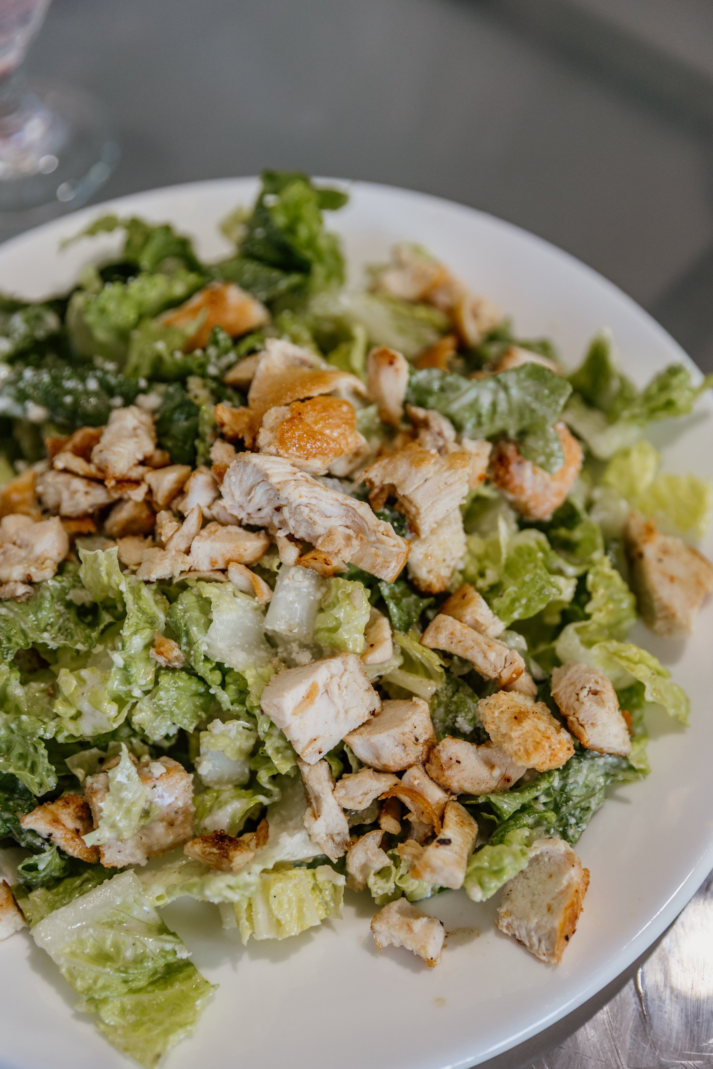 Caesar salad with chopped grilled chicken, romaine lettuce, grated cheese, and croutons on a white plate.