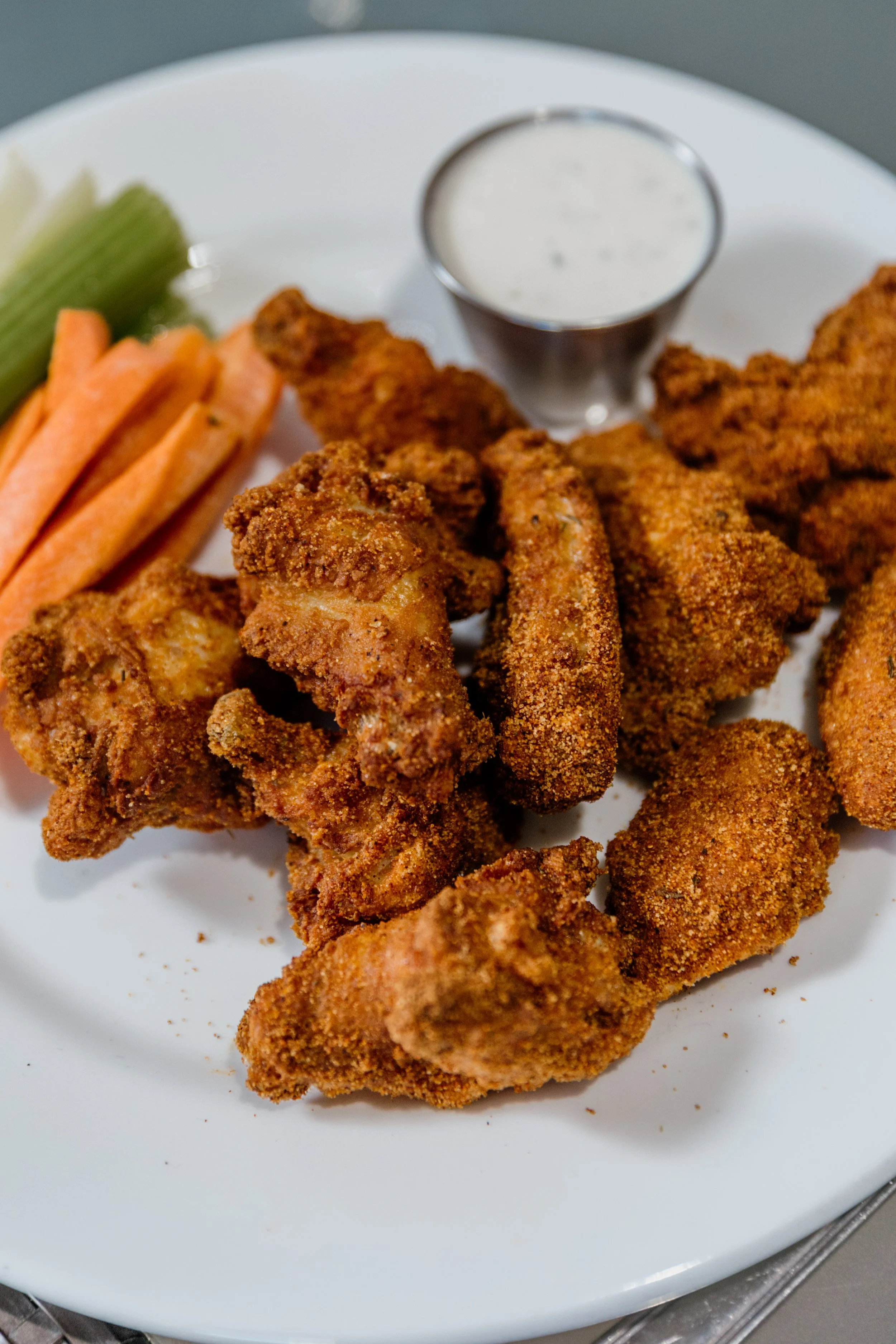 Plate of fried chicken wings with a side of celery and carrot sticks, and a cup of ranch dipping sauce.
