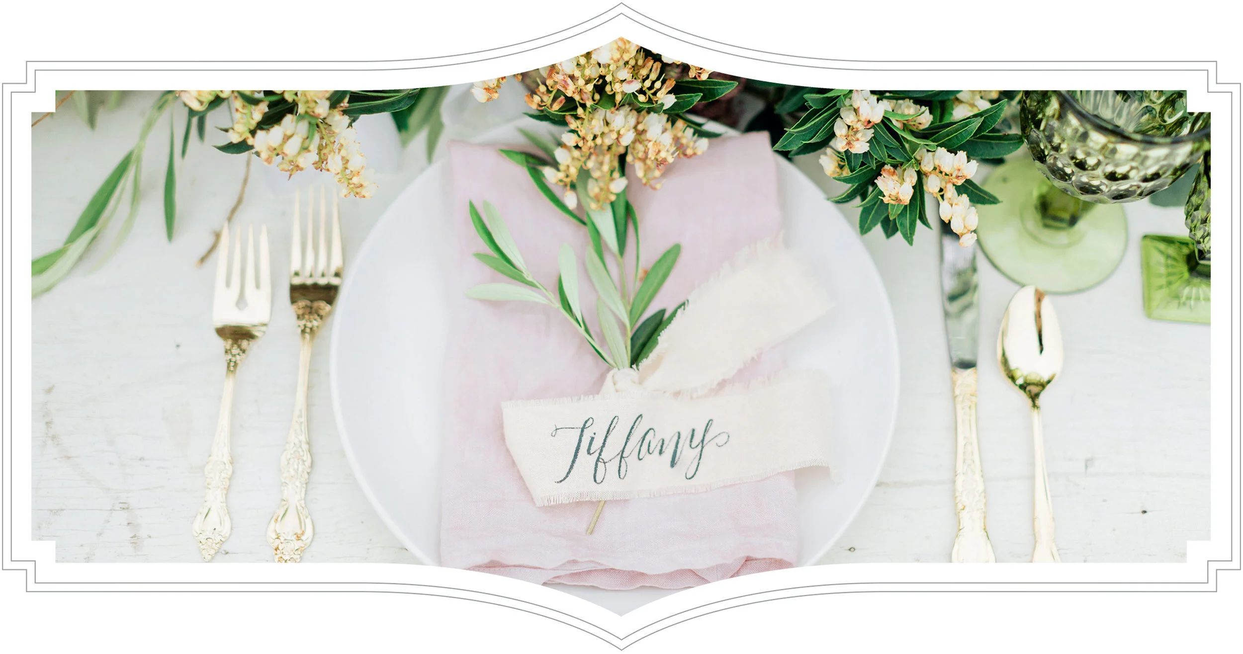 Elegant table setting with gold flatware, a white plate with a pink napkin and greenery, and a place card that reads 'Tiffany,' surrounded by floral arrangements in green and glass vases.