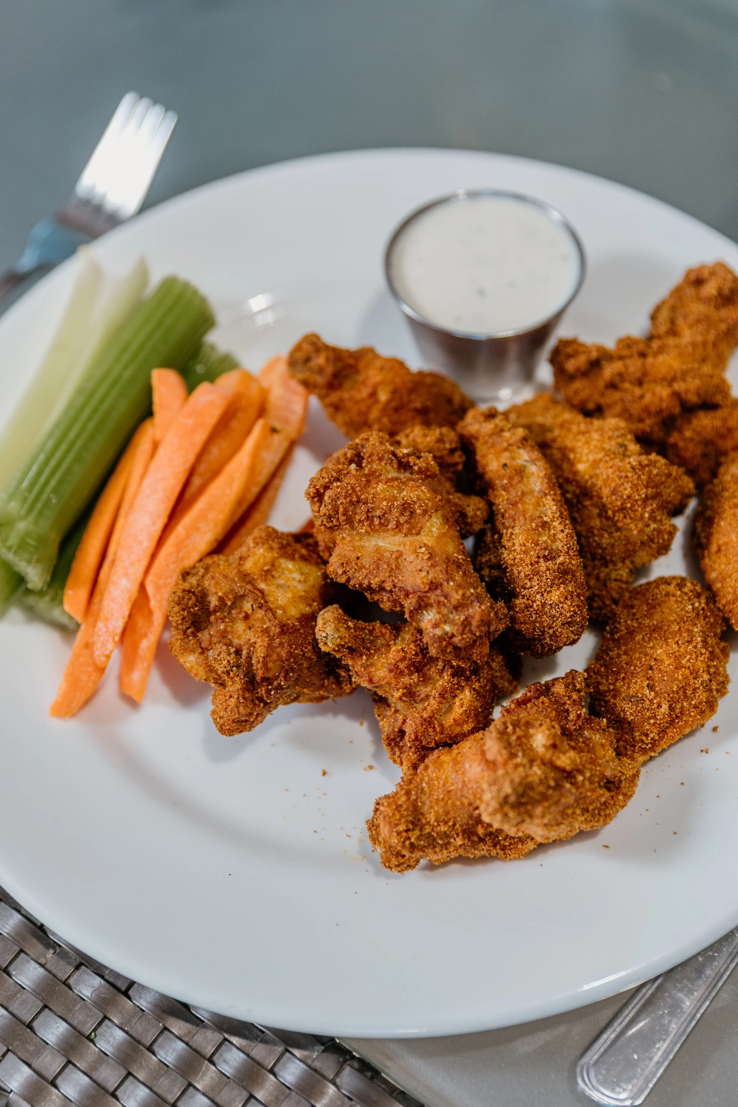 Fried chicken tenders served with celery and carrot sticks, ranch dressing, and a cup of white dipping sauce.