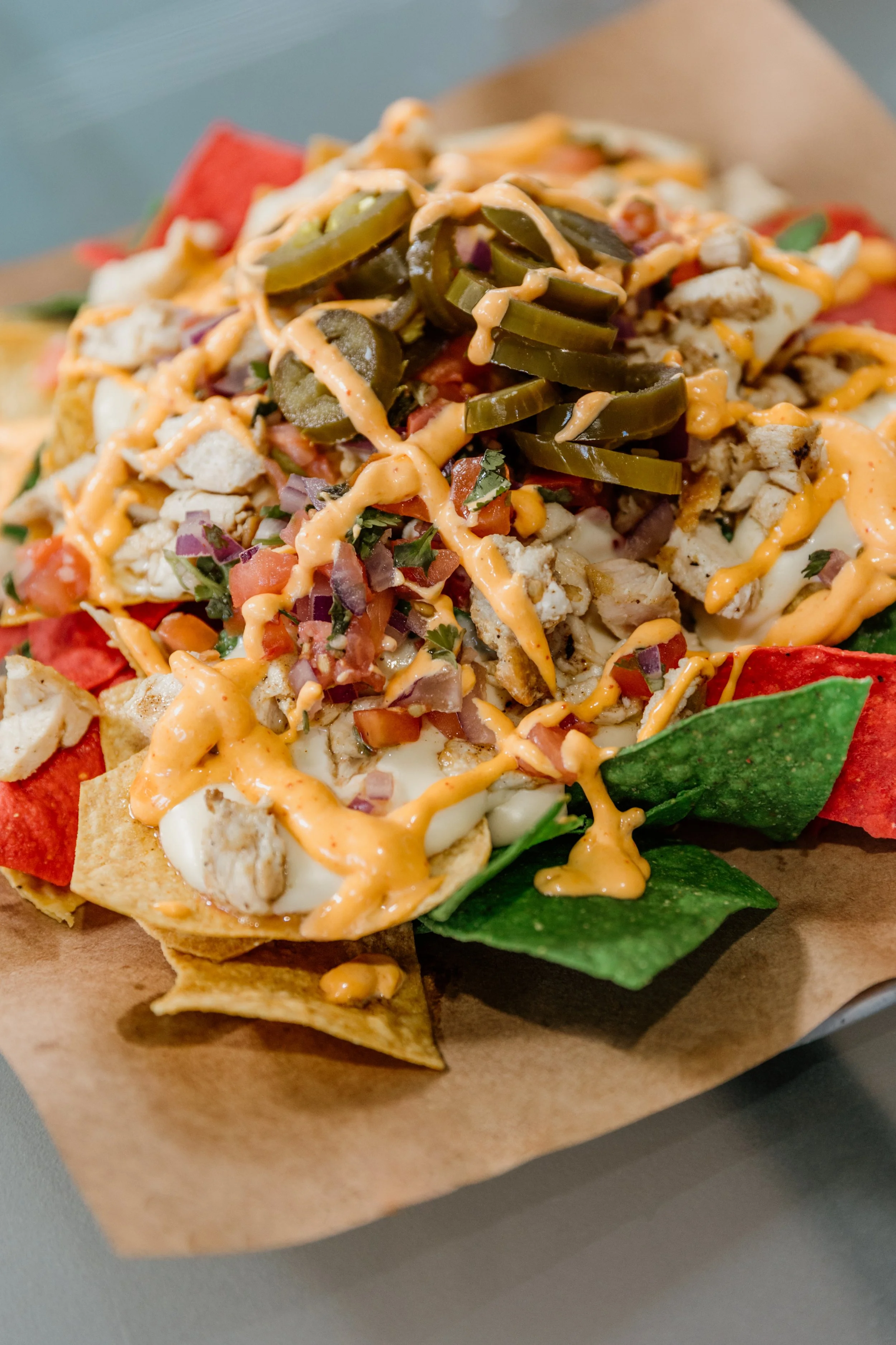 Loaded nacho dish with tortilla chips, shredded chicken, jalapeño slices, diced tomatoes, onions, and drizzled spicy orange sauce.
