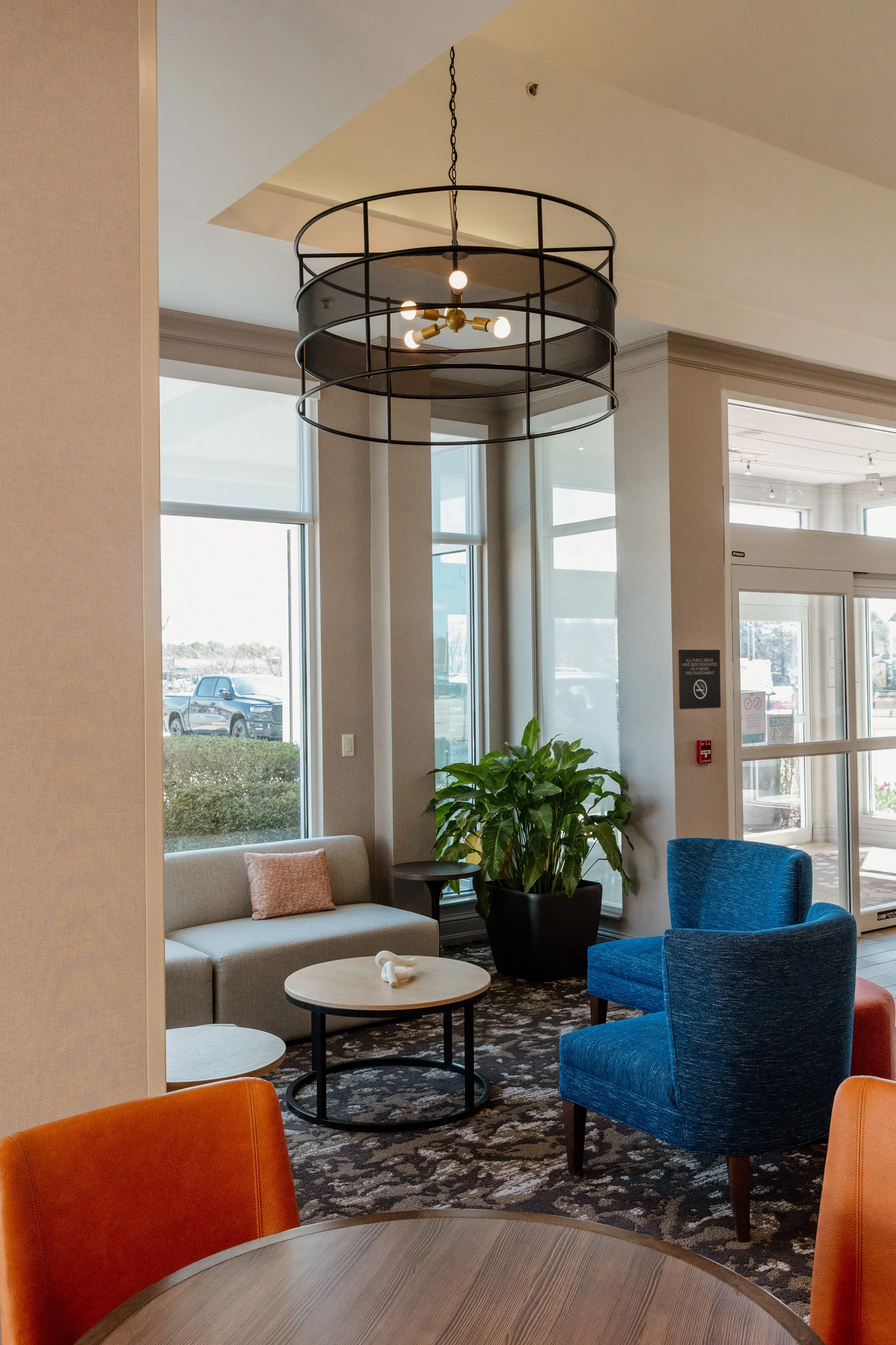 Modern hotel lobby with seating area, colorful chairs, a sofa, potted plant, and a contemporary chandelier ceiling light.