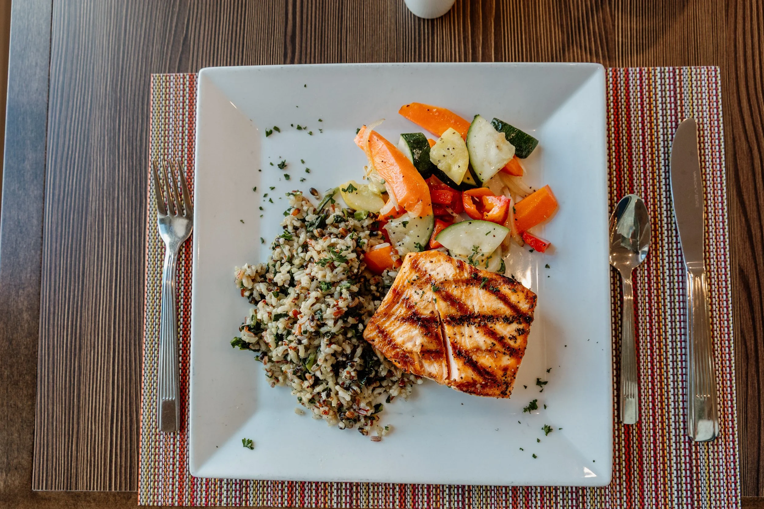 Grilled salmon served with sautéed mixed vegetables and rice on a square white plate.