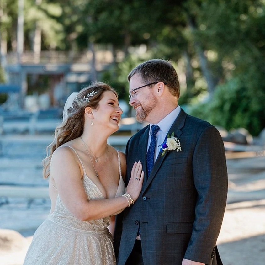 A bride and groom share a joyful moment outdoors, smiling and looking into each other's eyes.