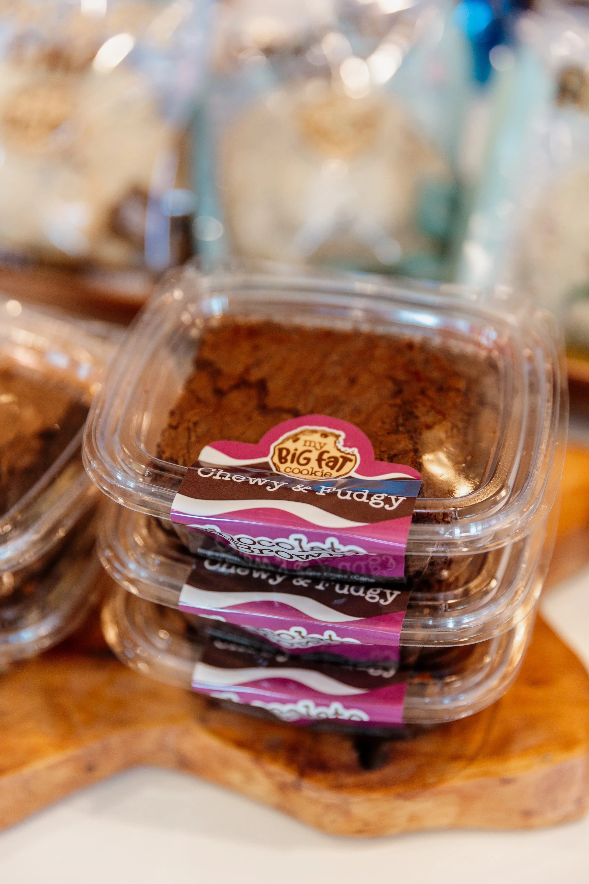 Stack of chocolate chip cookies labeled 'Chewy & Fudgy' from Big Fat Cookies, placed on a wooden serving board.