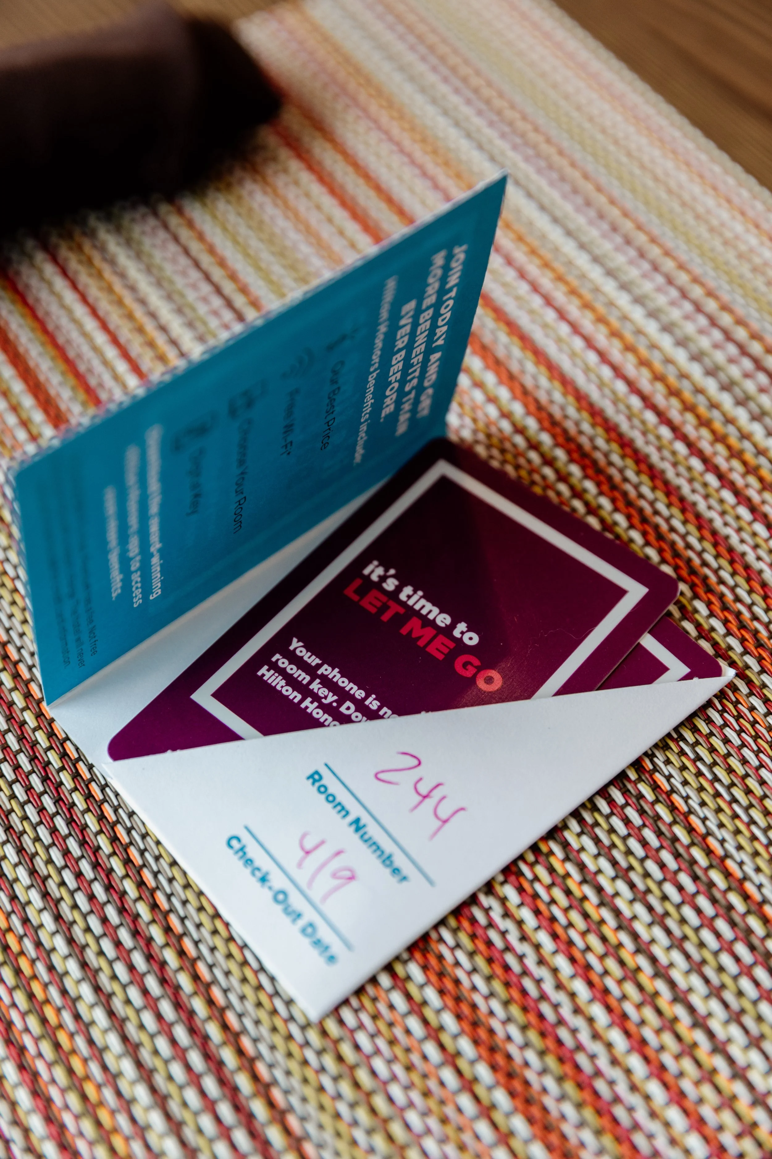 Hotel room key envelope with the room number 244 written in pink, and a card with a motivational message, on a colorful striped tablecloth.