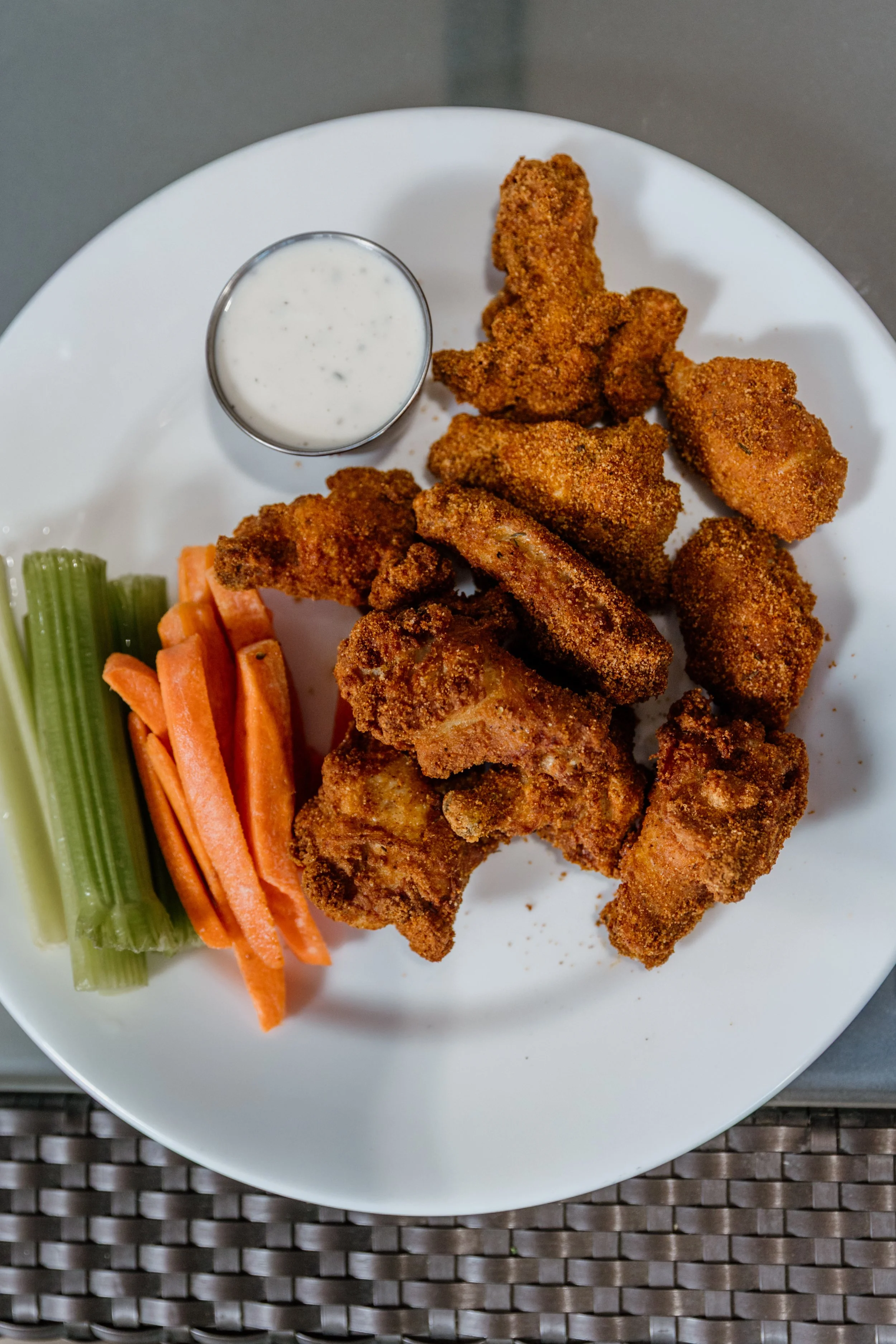 Fried chicken wings with dipping sauce, celery and carrot sticks on a white plate.