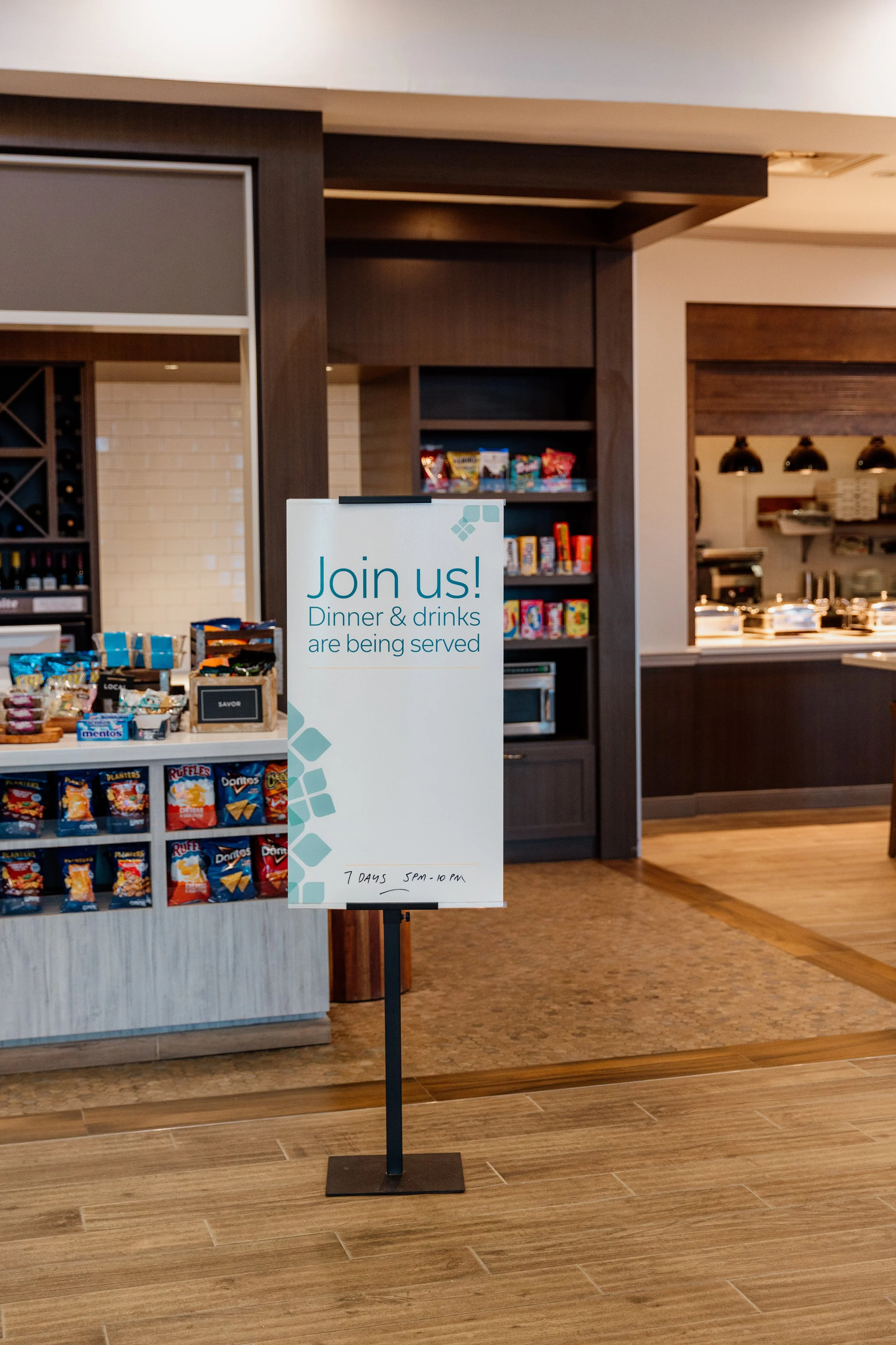 Sign inviting guests to dinner and drinks with snack display to the left and buffet area in the background.