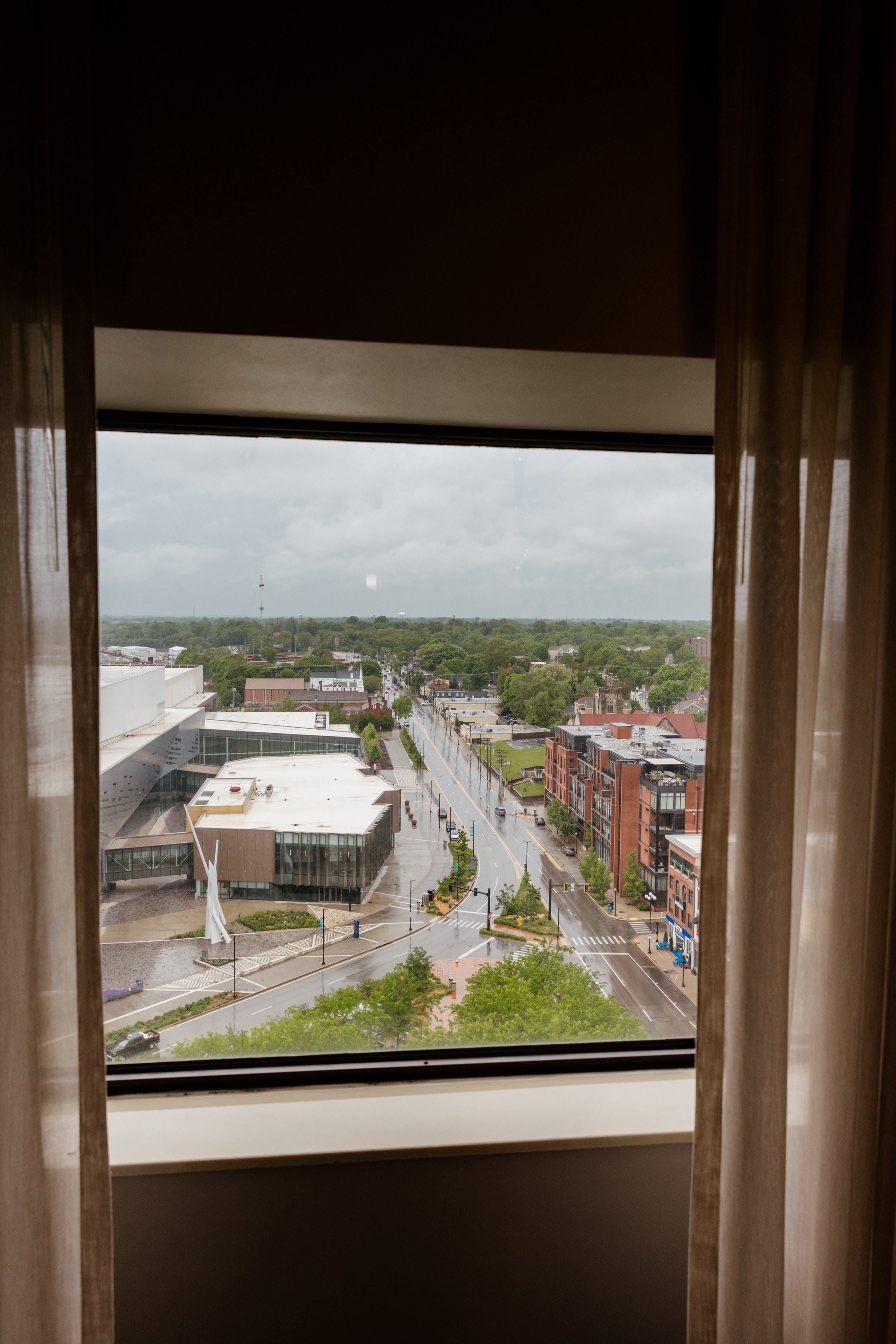 View of a city street and buildings through a window with curtains on each side.