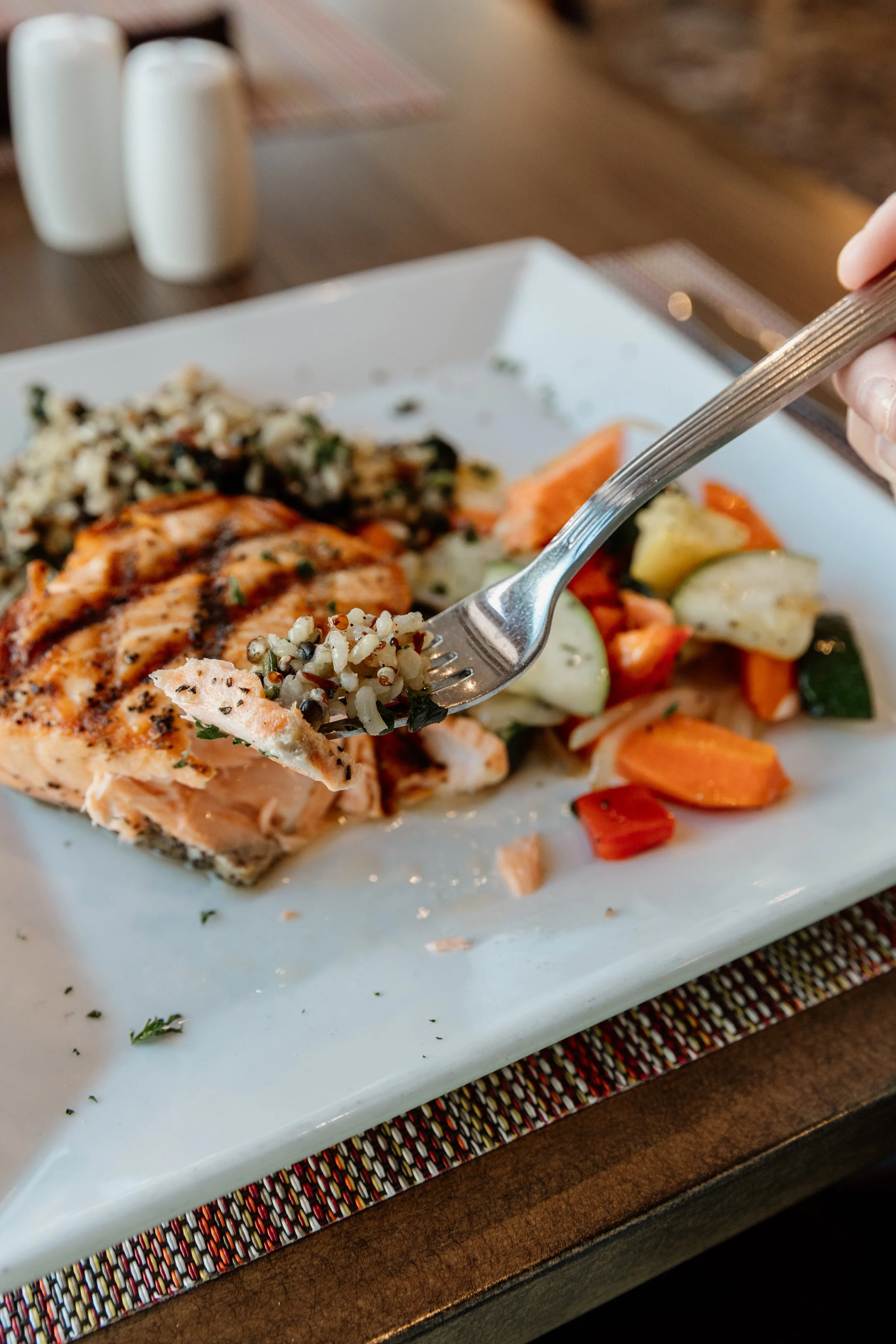 A plate of cooked salmon with rice, vegetables, and a slice of lemon, with a fork holding a bite of rice and fish.