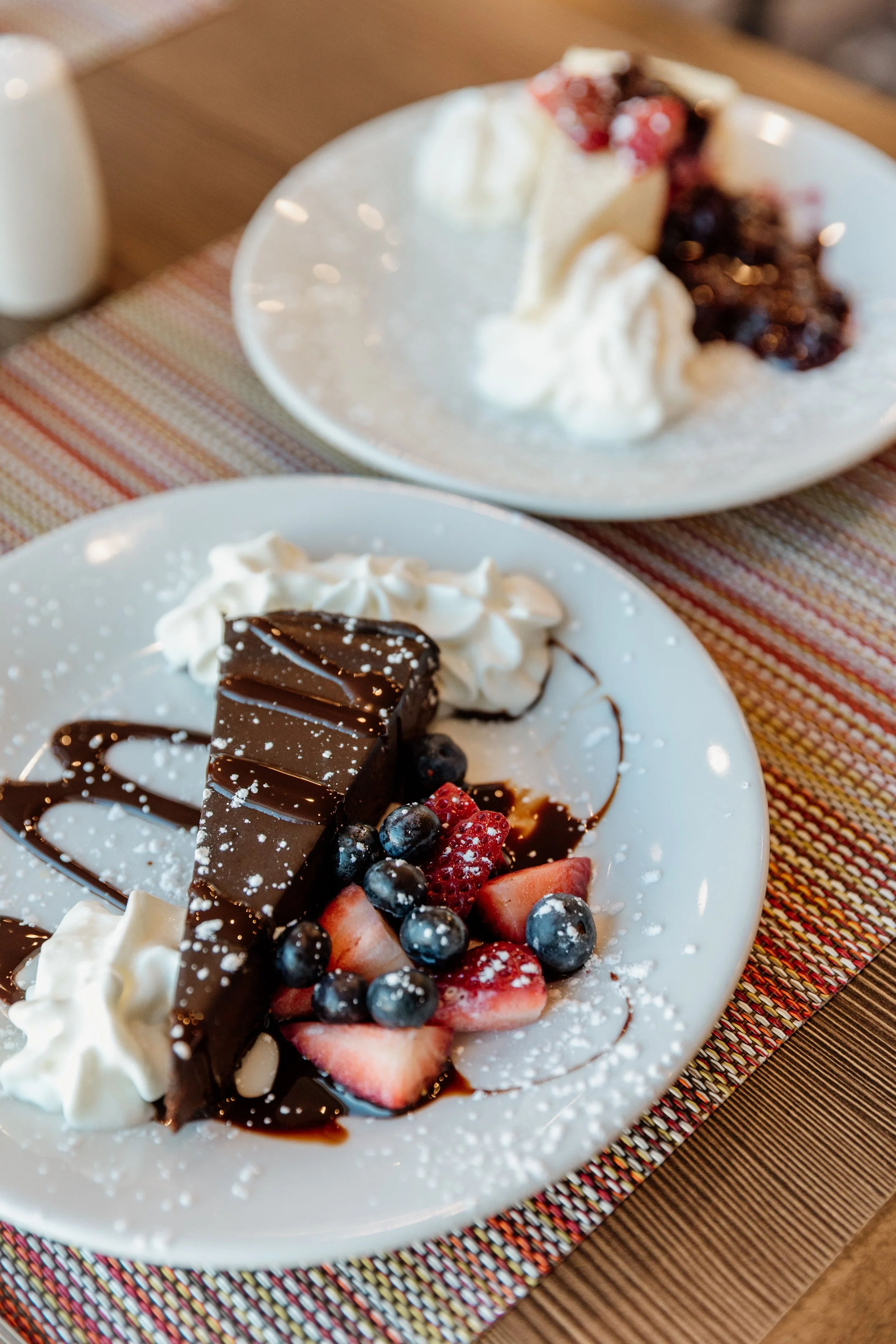 A dessert plate with a slice of chocolate cake, fresh strawberries, blueberries, whipped cream, and chocolate sauce.