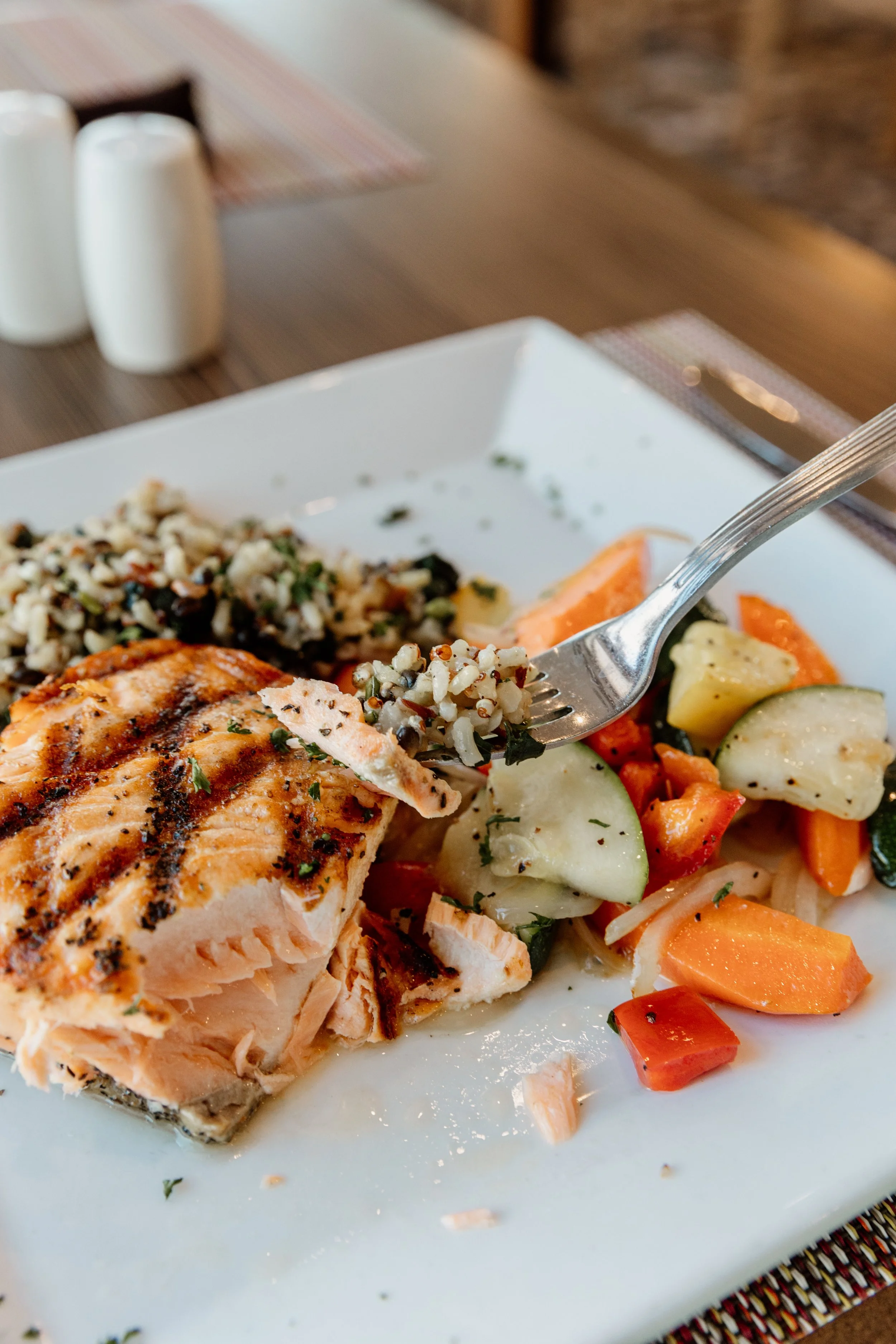 Close-up of a plate with grilled salmon, mixed grilled vegetables, rice, and quinoa salad.