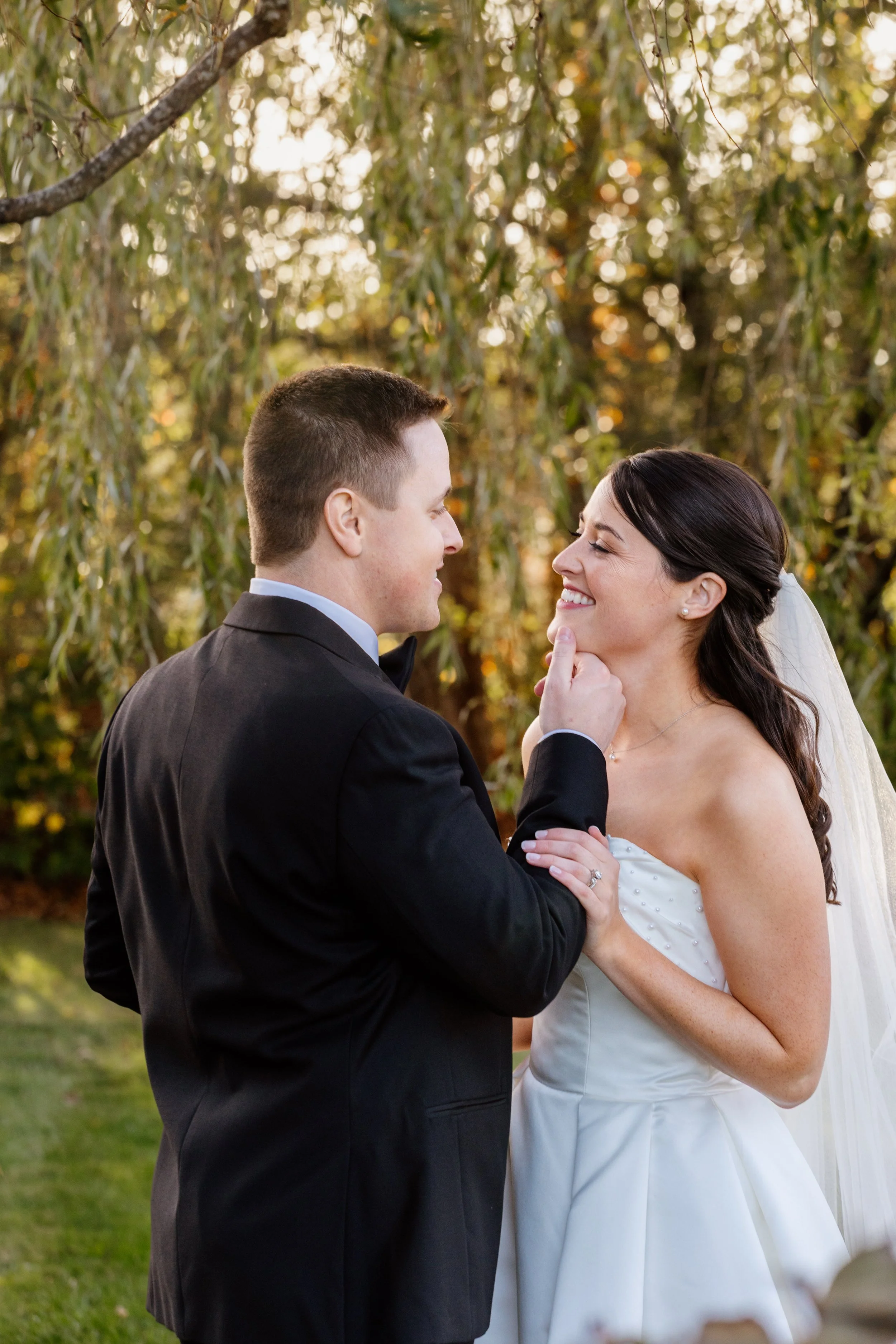 A candid moment between a bride and groom just before their reception at The Hounds in Stonington, Connecticut, the groom gently tilting her chin as they share a smile in the warm sunset light.