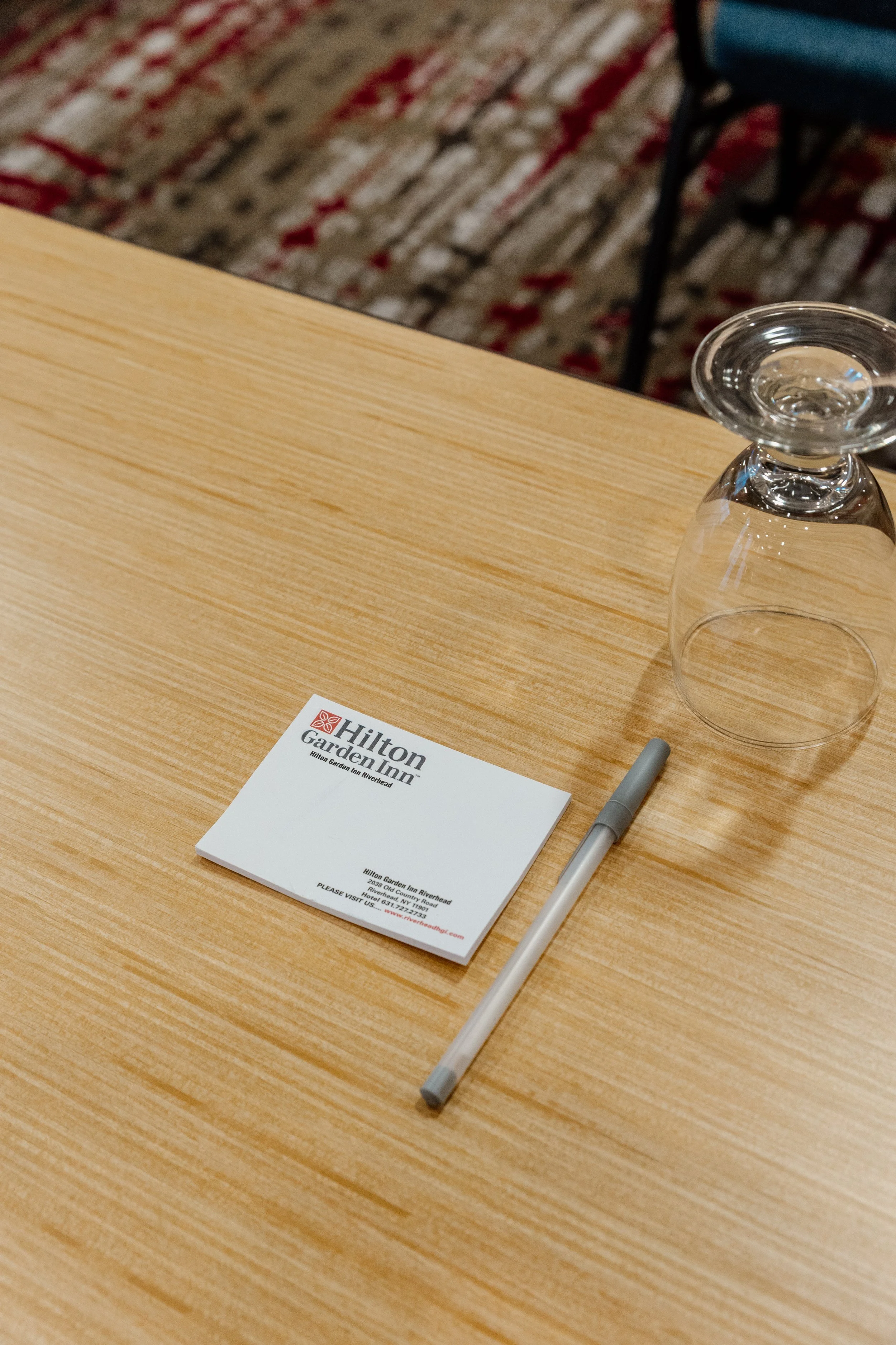 A wooden table with a Hilton Garden Inn note card, a gray pen, and an upside-down glass.