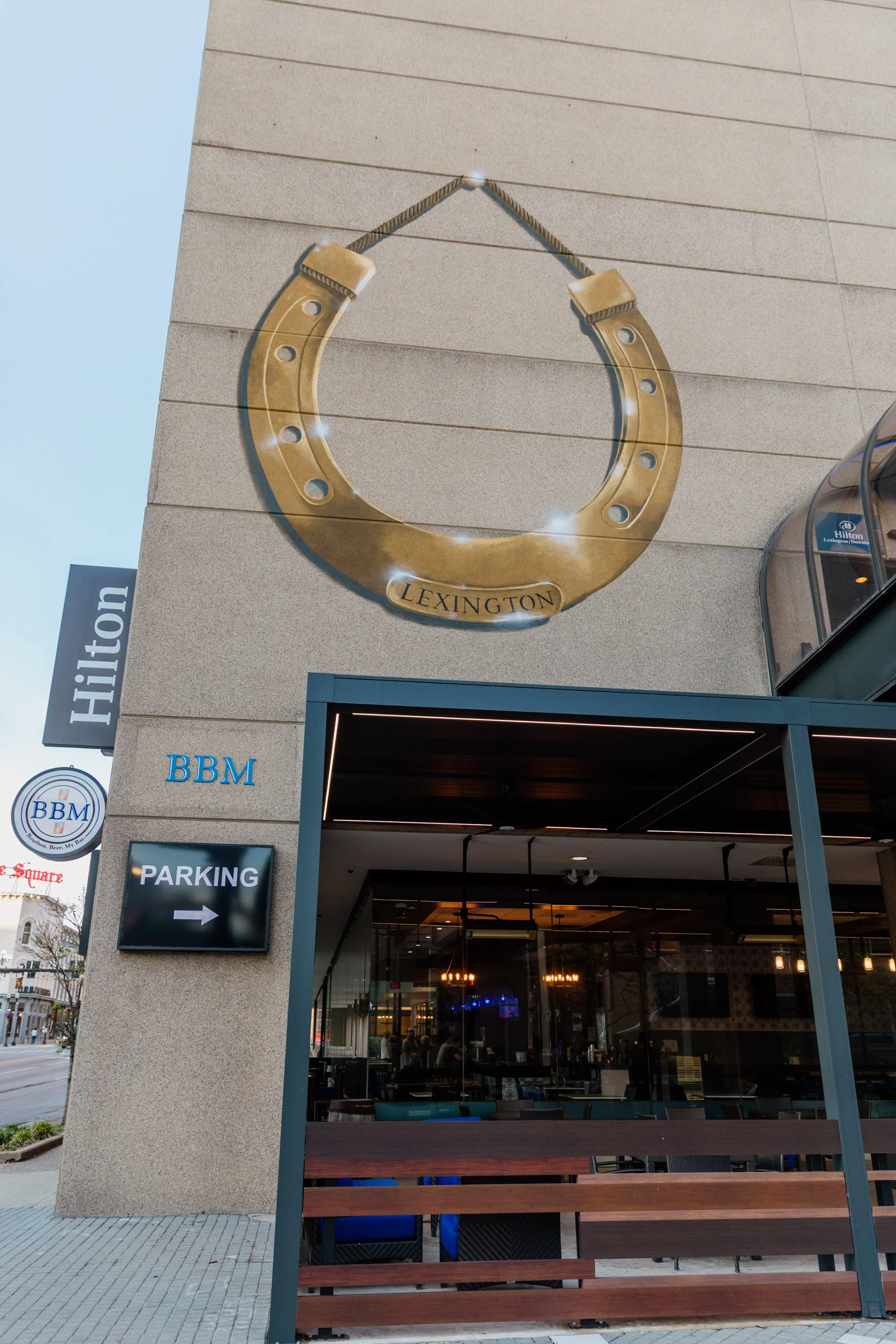 Outdoor view of the Lexington hotel showing a large horse shoe decoration, hotel signs, and a restaurant seating area.