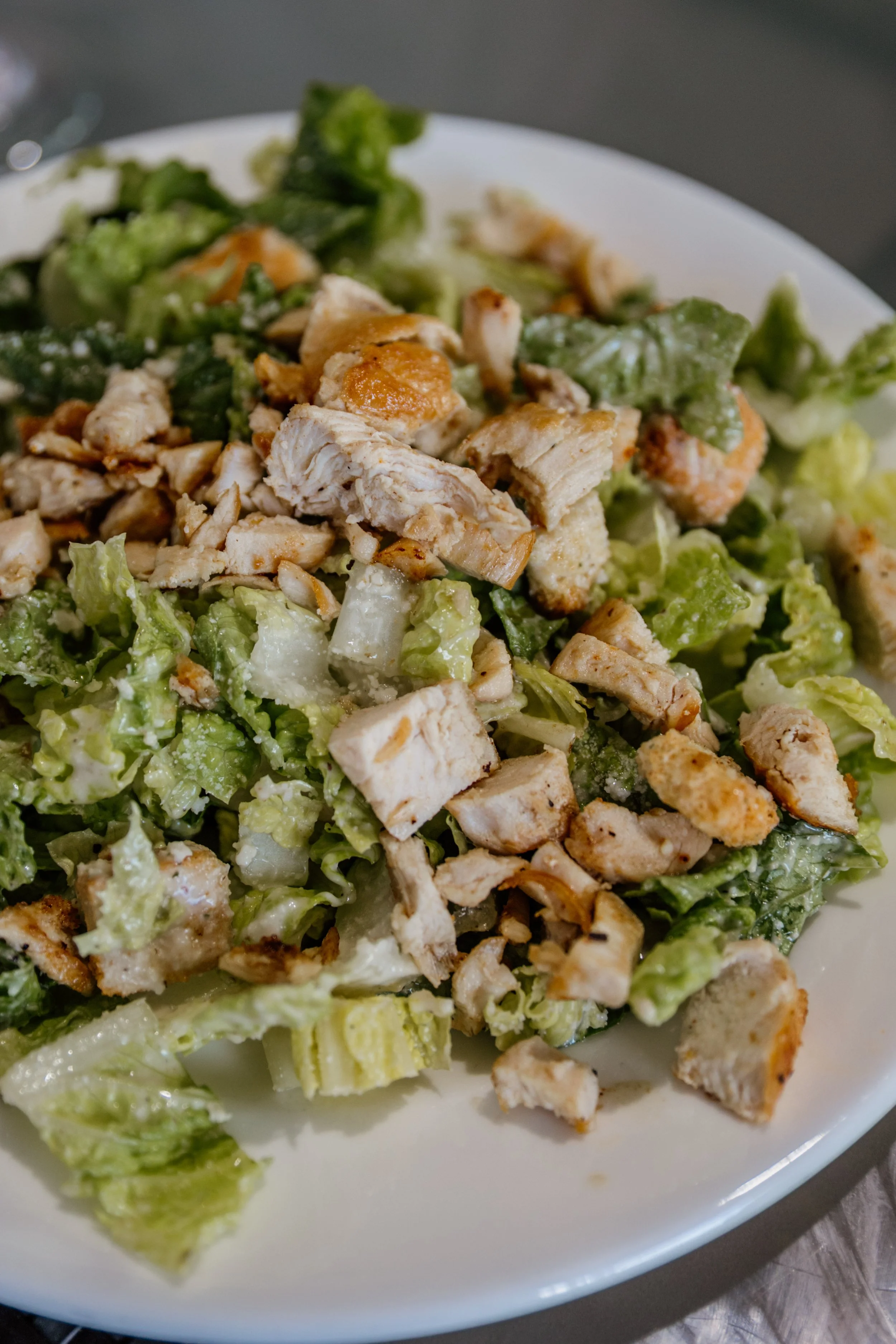 Caesar salad with chopped grilled chicken on a white plate.
