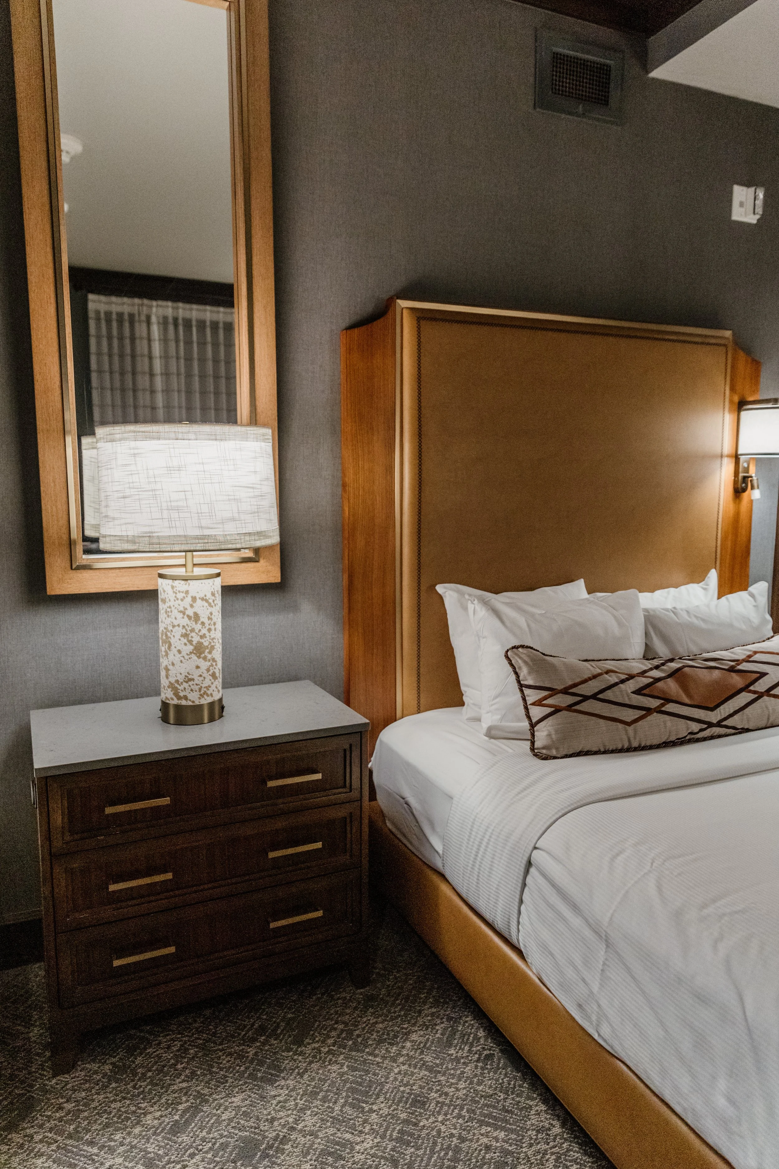 A hotel room with bed, bedside table, lamp, and mirror.