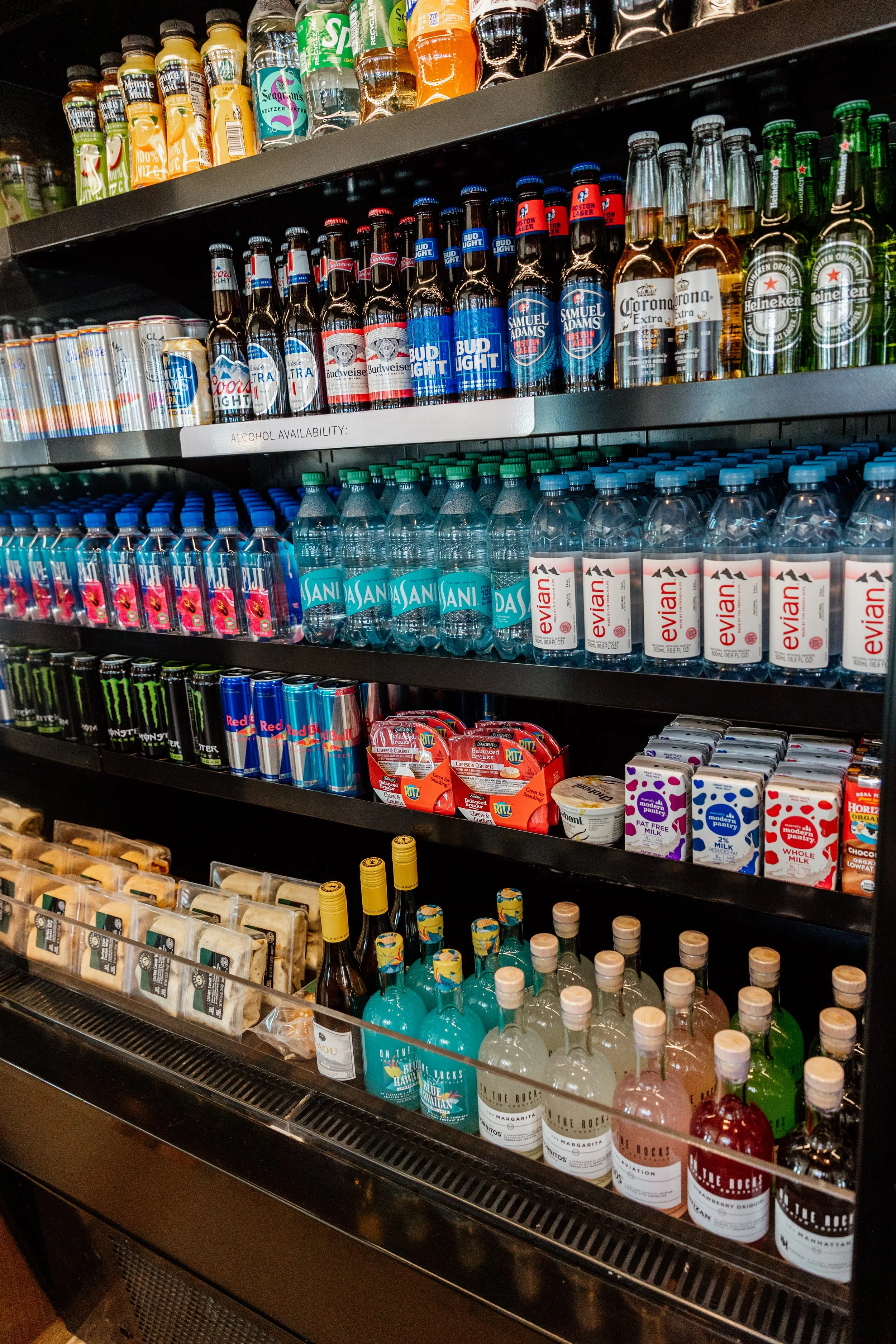 Shelf stocked with a variety of bottled drinks including beers, water, juices, and alcoholic beverages.