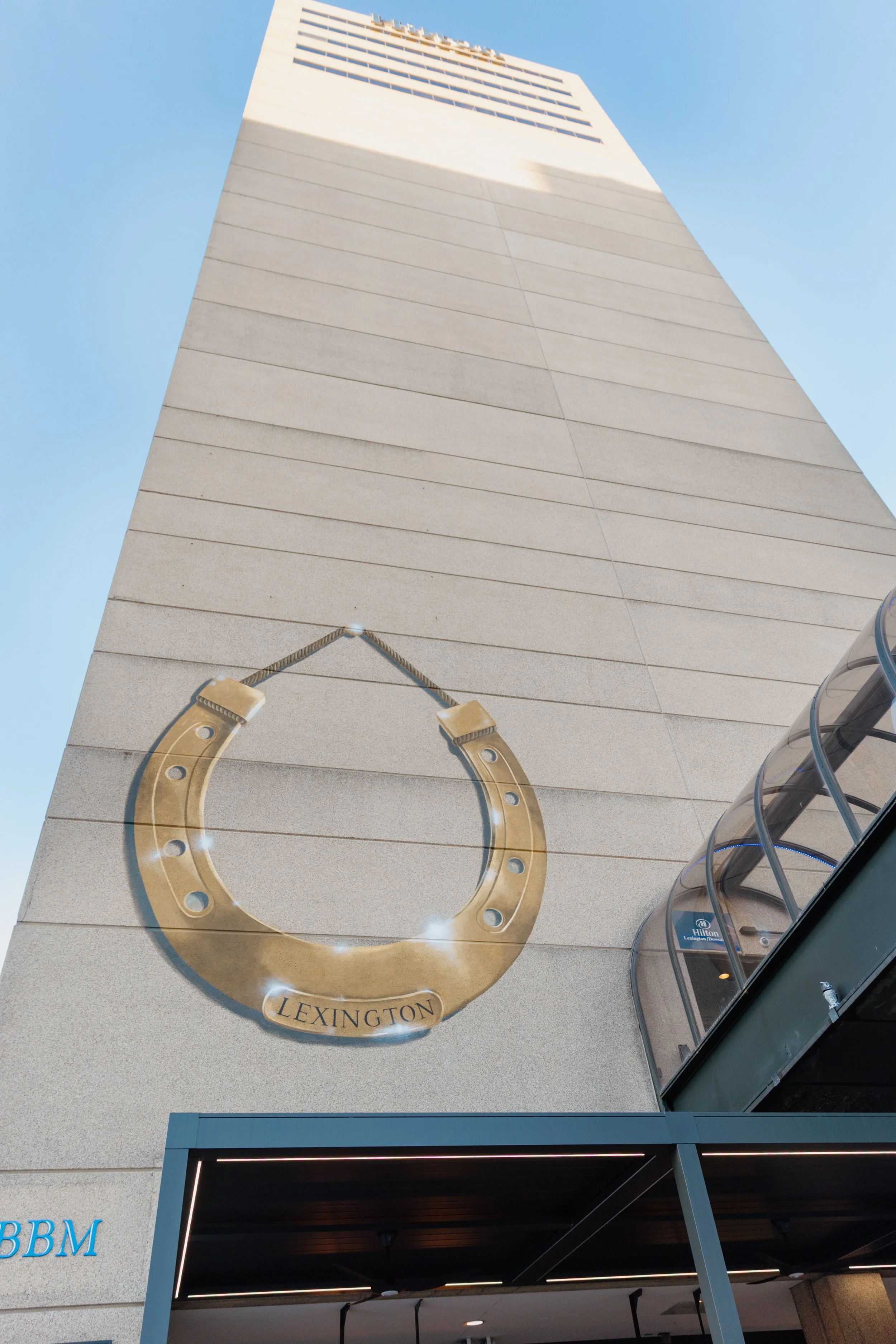 A tall building with a horse shoe decoration that has the word "Lexington" on it, and a sky and hotel entrance visible.