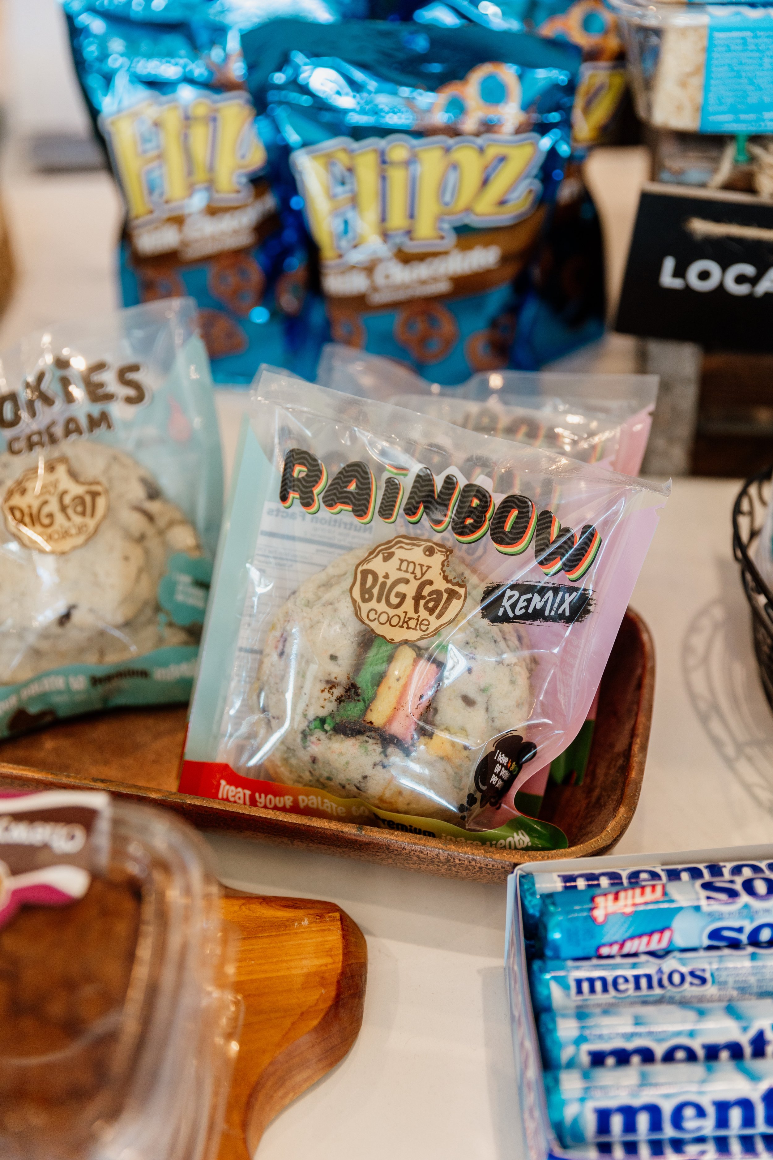 Variety of cookies and snacks on a table, including Rainbow my big fat cookie, Flipz pretzels, Mentos mints, and other snack packages.