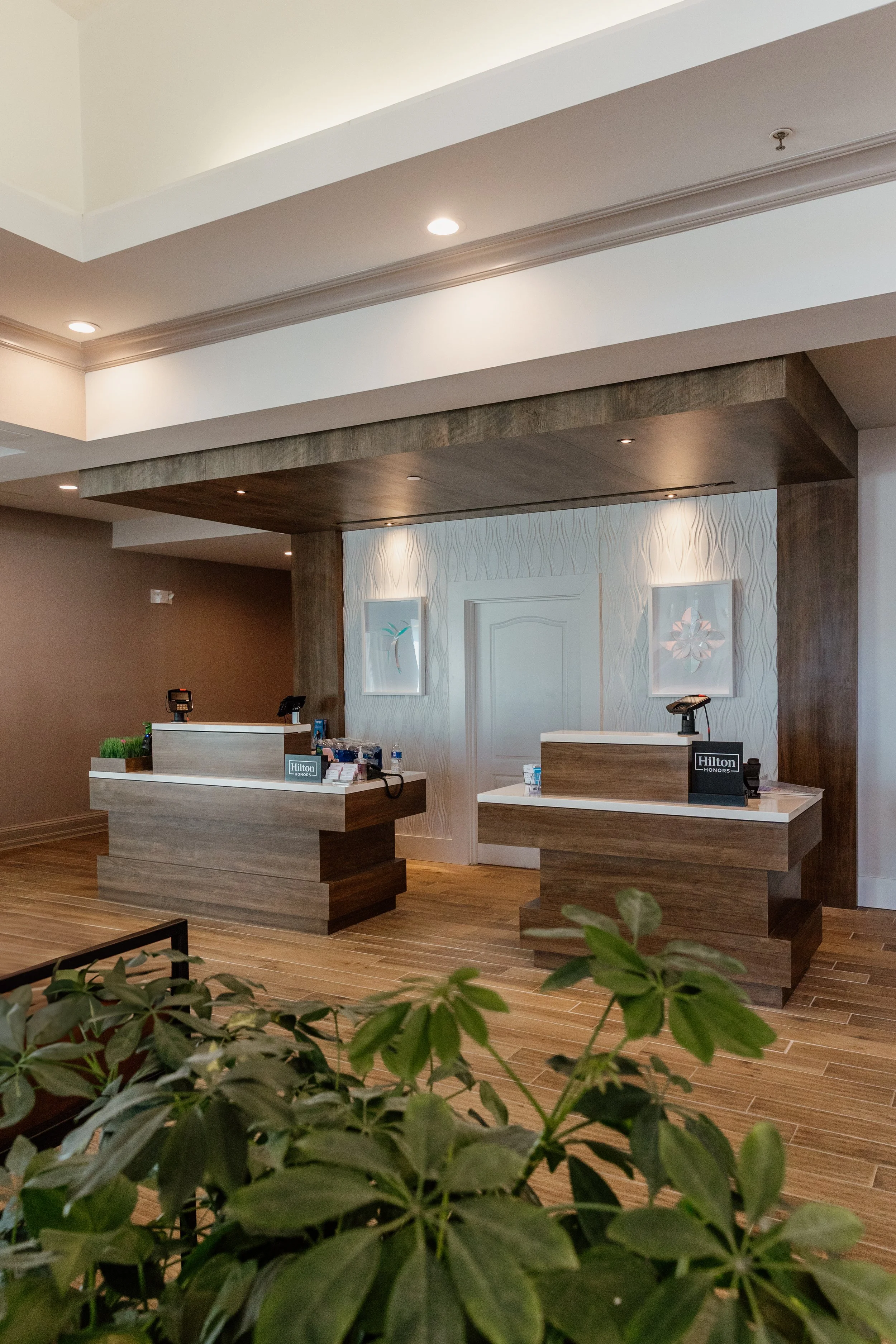 Hilton hotel check-in counters with two desks, digital scanners, and small benches or plants in front, inside a modern lobby