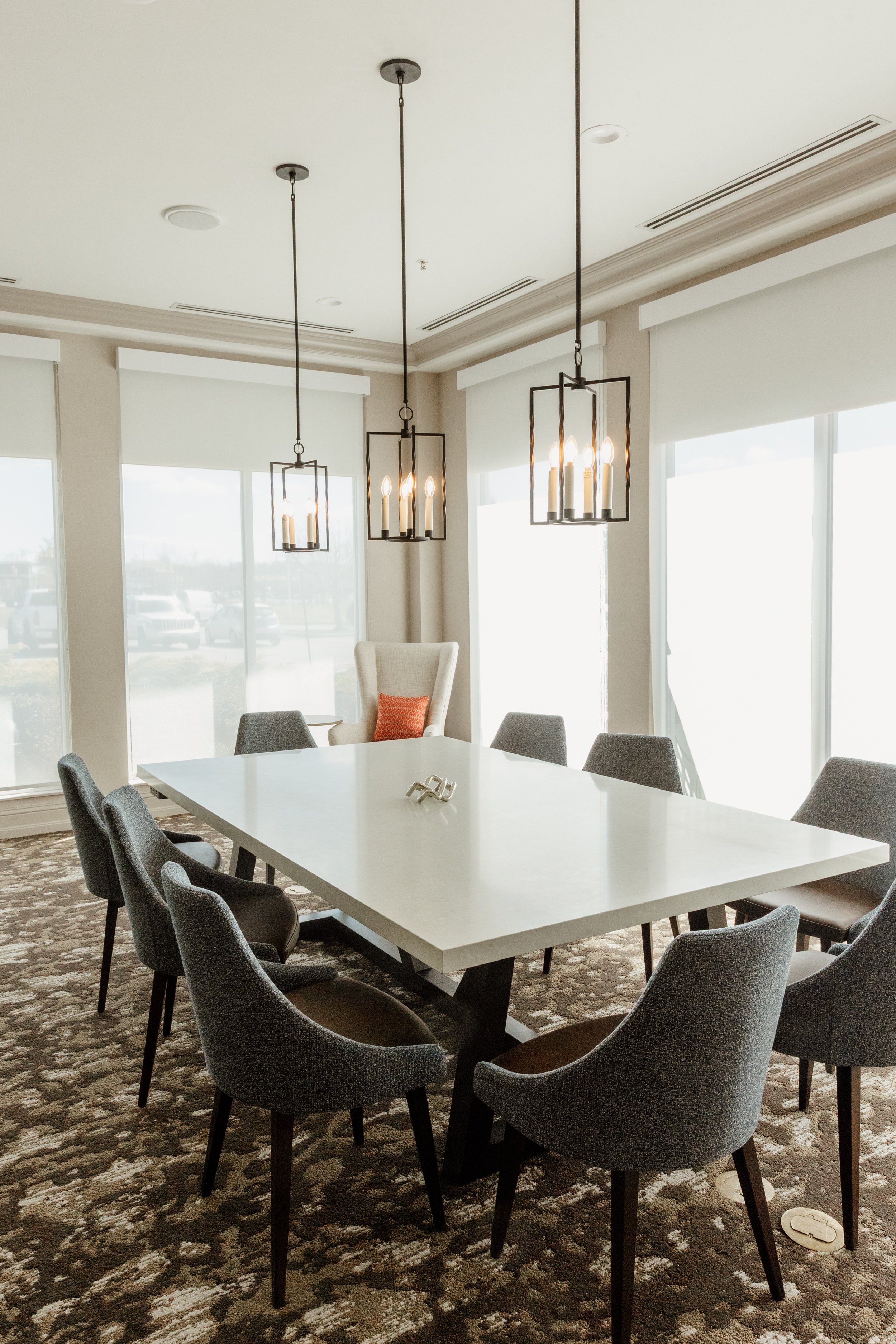 Modern conference room with white table, grey chairs, and hanging pendant lights.