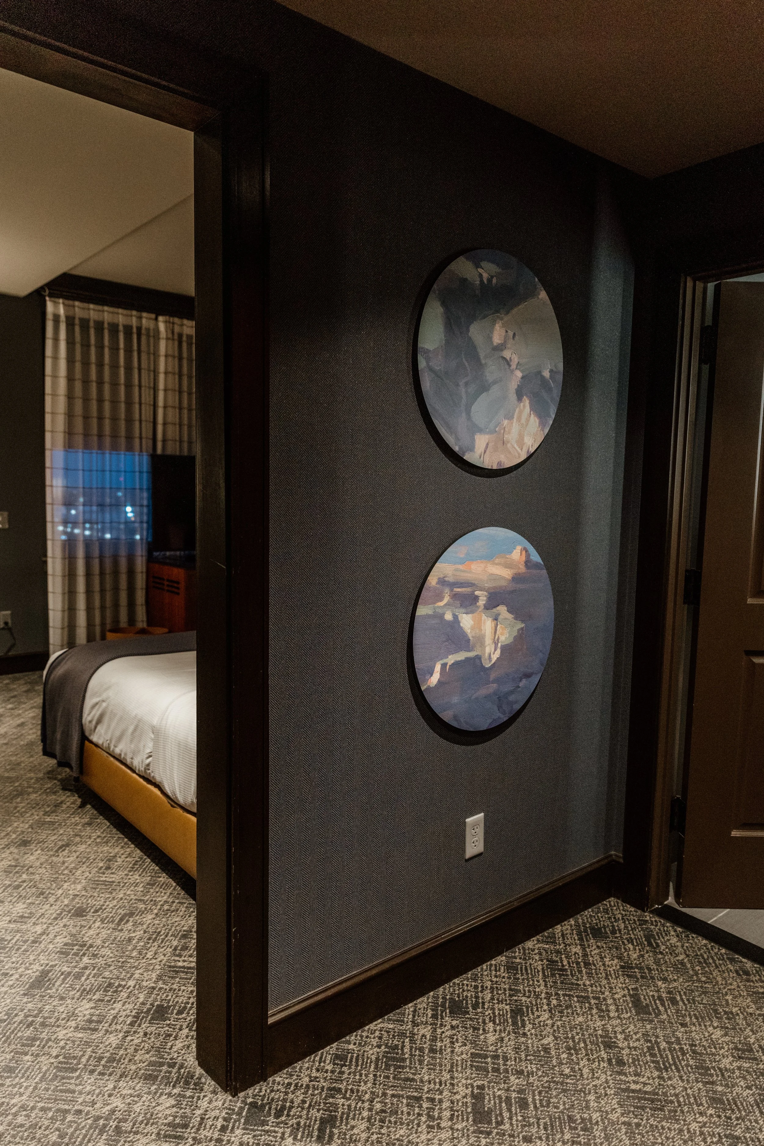 Two circular landscape paintings hanging on a dark wall near a doorway, with part of a bedroom visible to the left.