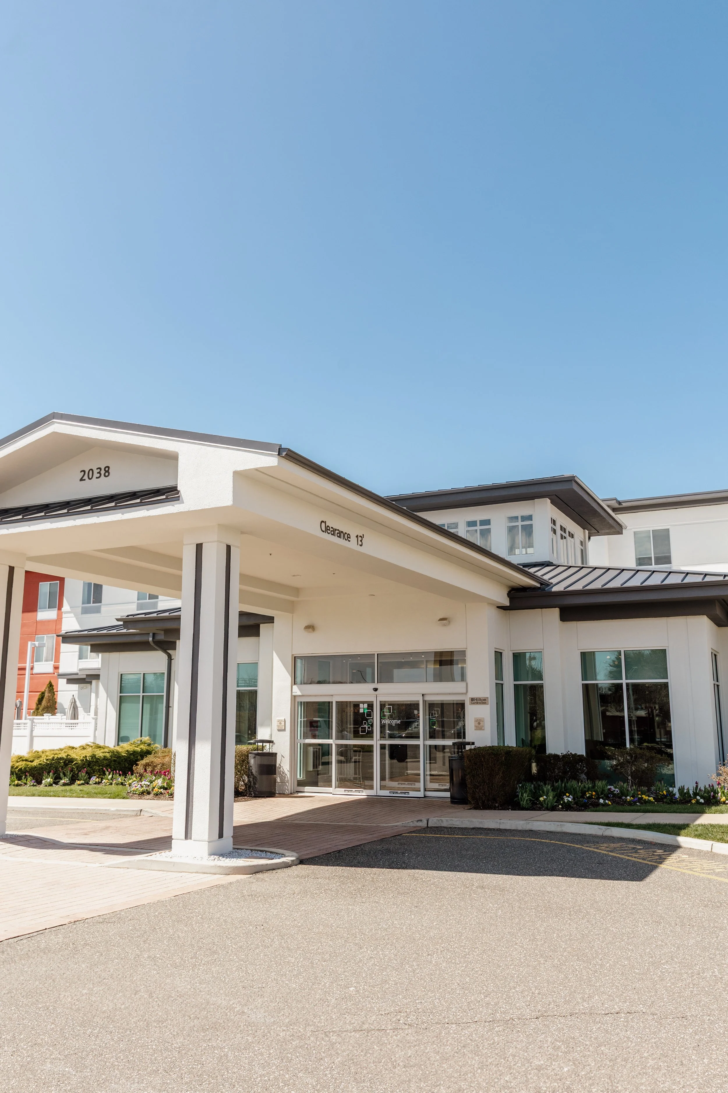 Residential apartment complex entrance with glass doors, landscaping, and a clear blue sky.