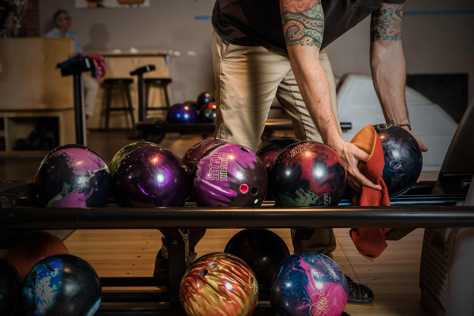 Colorful bowling balls being picked up by man with tattoos