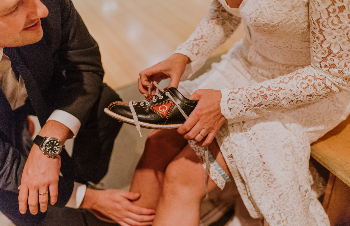 Bride laces bowling shoes with watchful groom