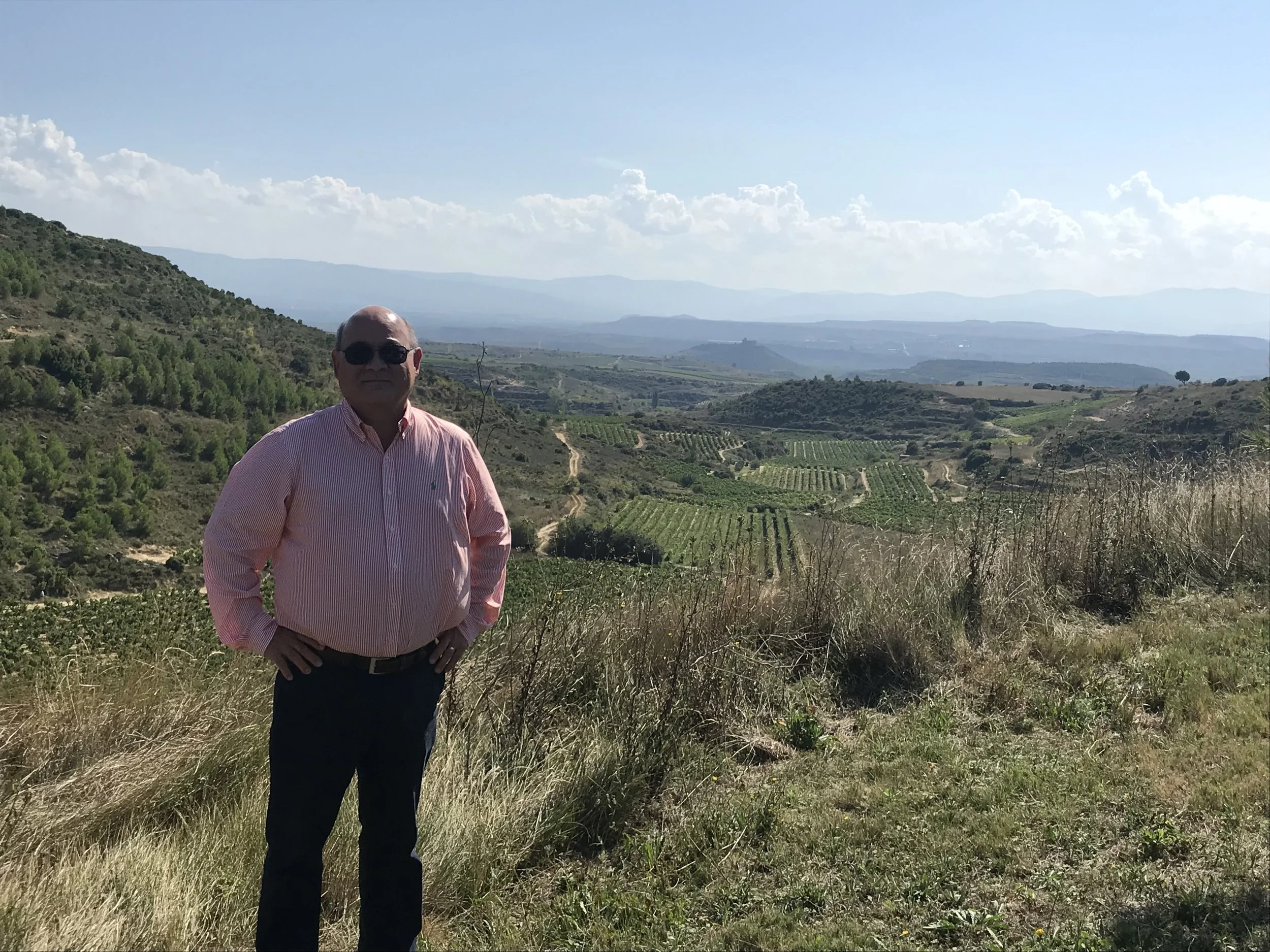 Standing on the grounds of Santa Maria de la Piscine with vineyards below and mountains in the distance.