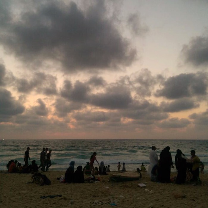 KHAN YOUNIS | Sun sets in Khan Younis as families relax together by the beach. From the far left, the twinkle of Israeli naval boats dot the horizon. July 11, 2016.