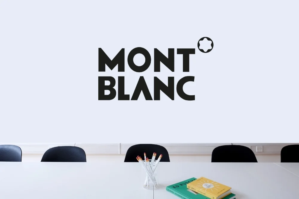 Mont Blanc logo on a white wall with a conference table and chairs beneath it.