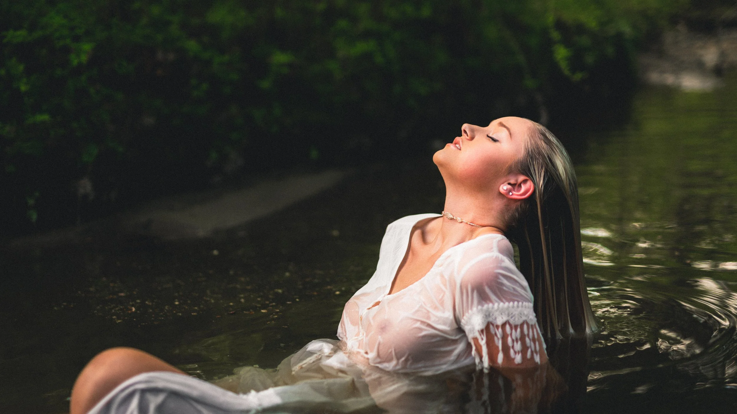 Woman reclining in water with long hair flowing in lush greenery