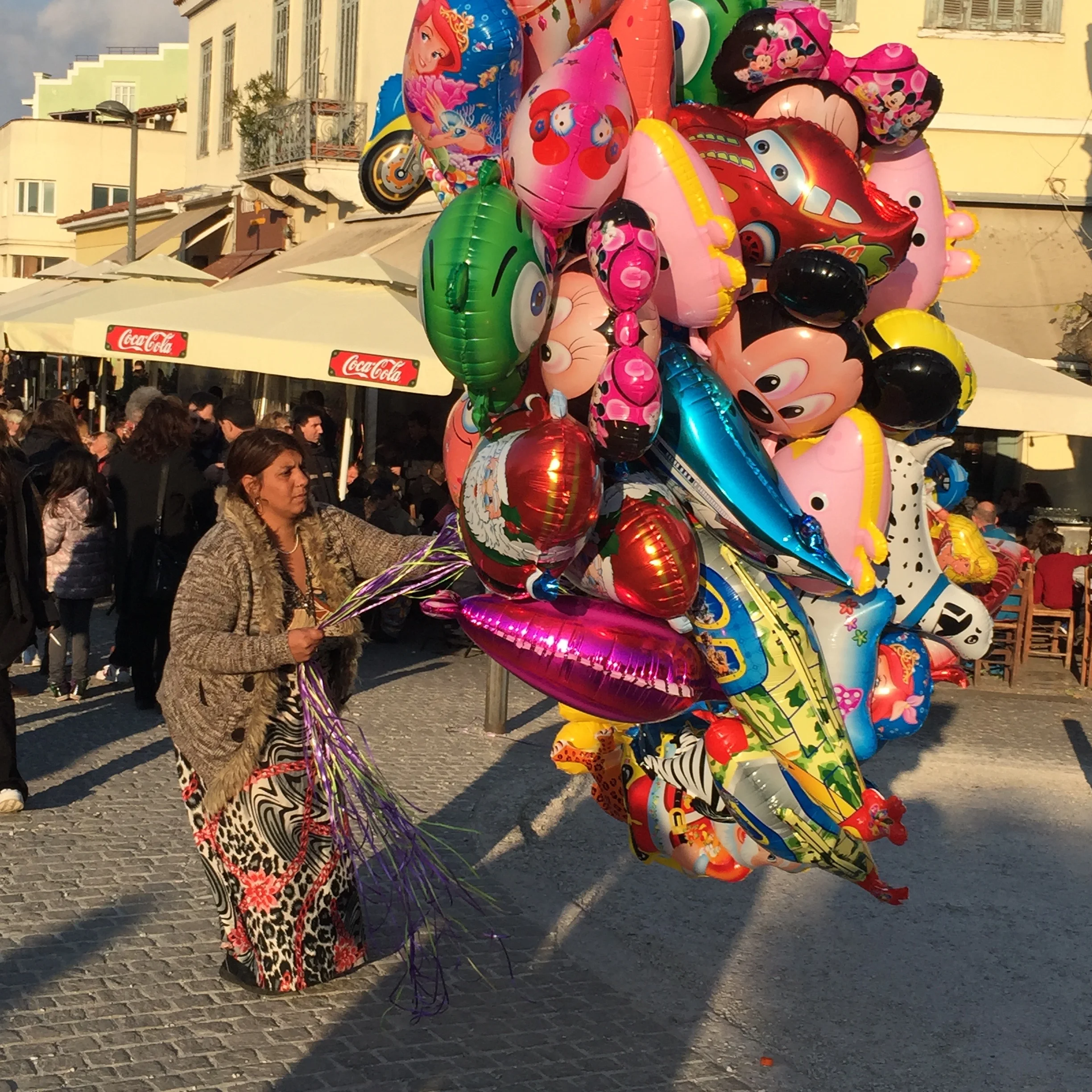 image: Athens, Greece 2014. A Gypsy woman and her balloons. Watching her made me want to cry. The winds were high and she struggled right and left to maneuver the colorful bunch, yet she could not sell any. 