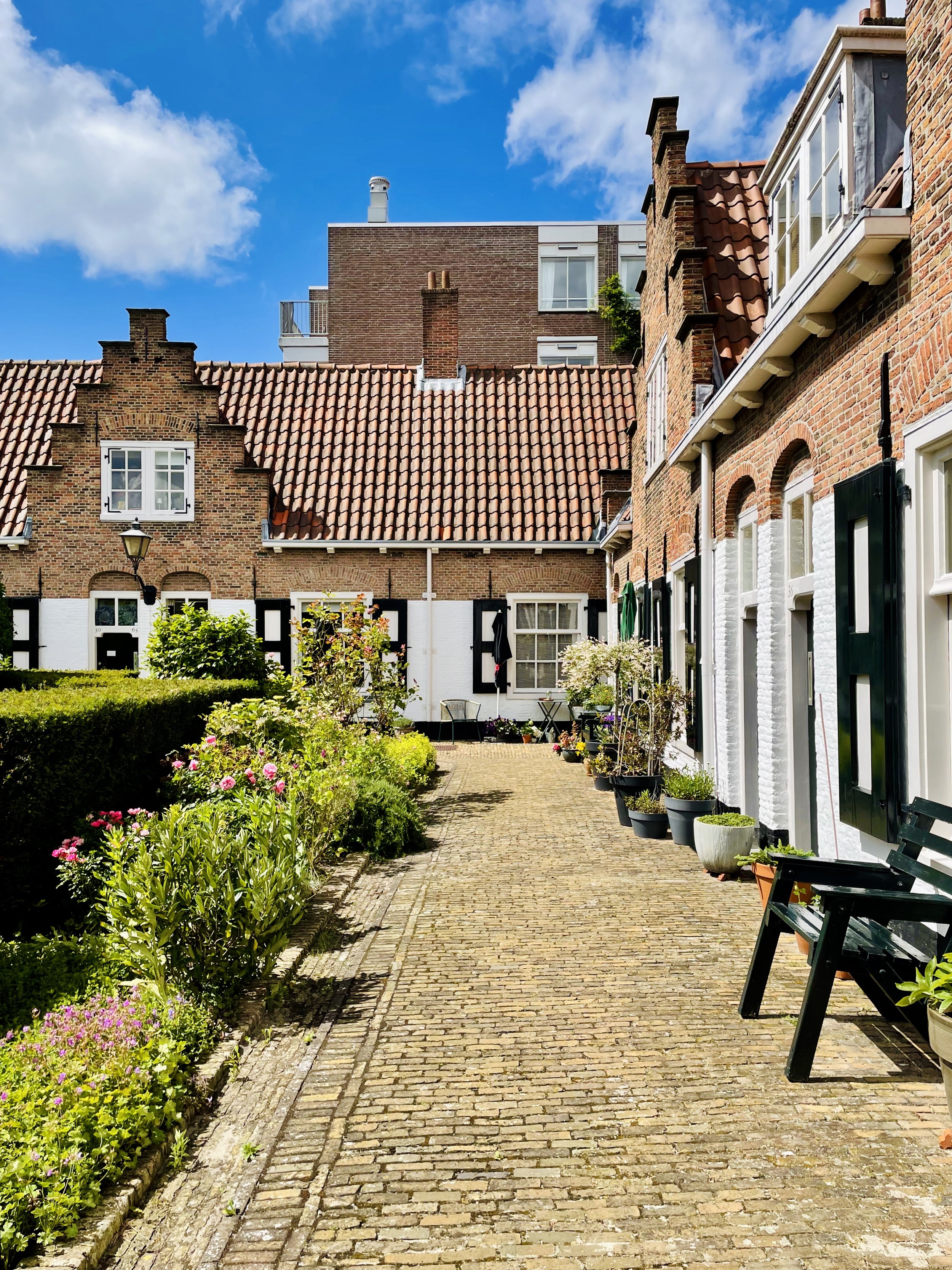 European brick courtyard with flower-lined path and Dutch gabled homes showing human-scale, garden-focused living.