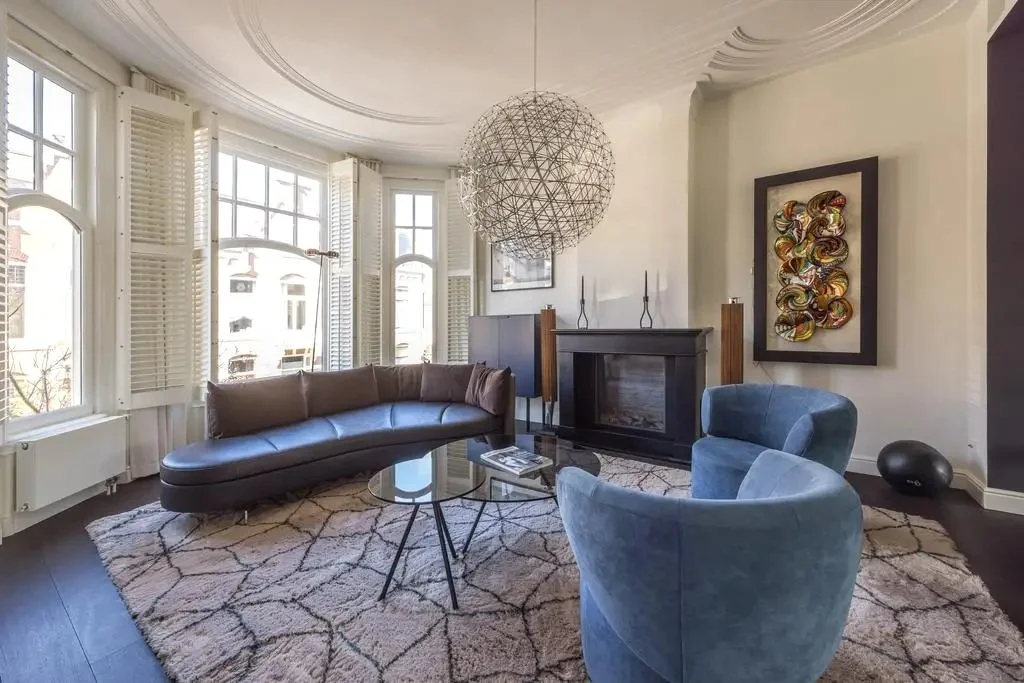 Dutch design approach to intentional living living room with bay windows, curved seating, and modern art in soft natural light.