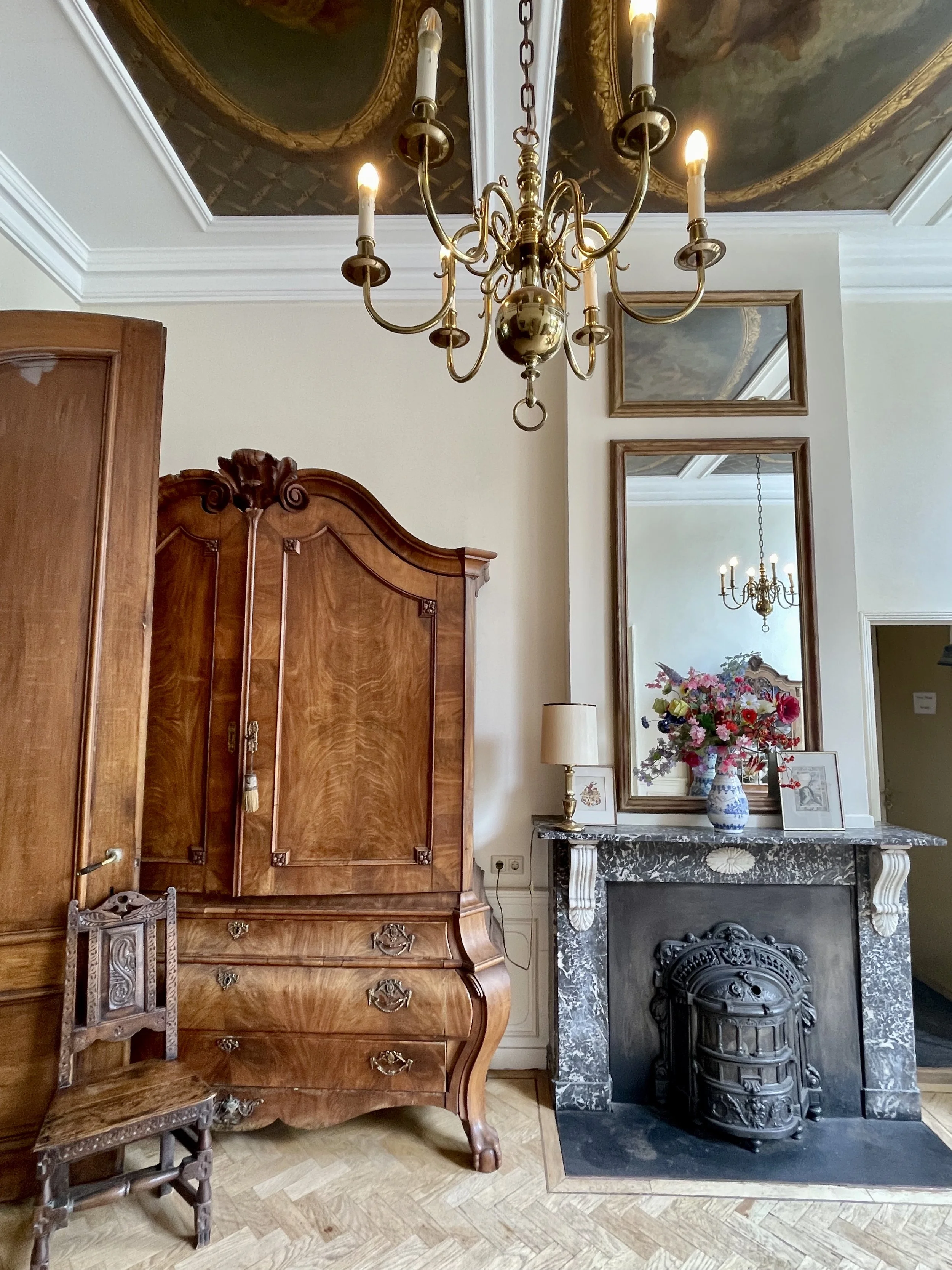 Historic European room with carved wood armoire, marble fireplace, and floral arrangement