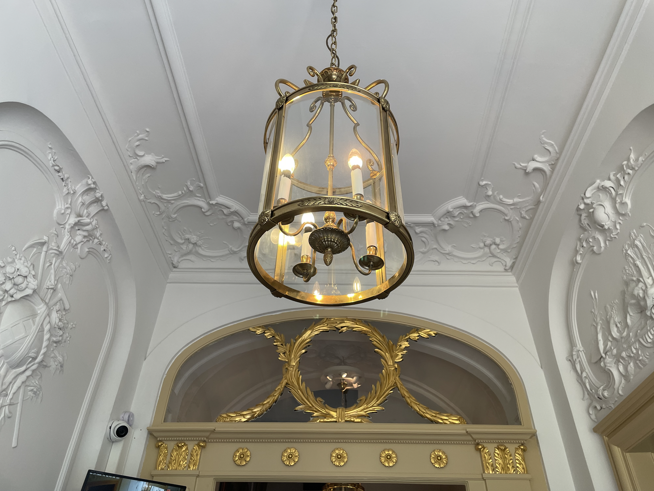 Historic European entry with hanging brass lantern, white plaster relief walls, and gilded architectural detailing