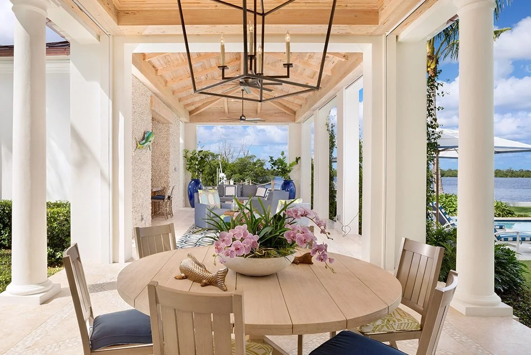 This columned loggia has dining in foreground with round teak wood table and chairs, with seating area closer to the sea.